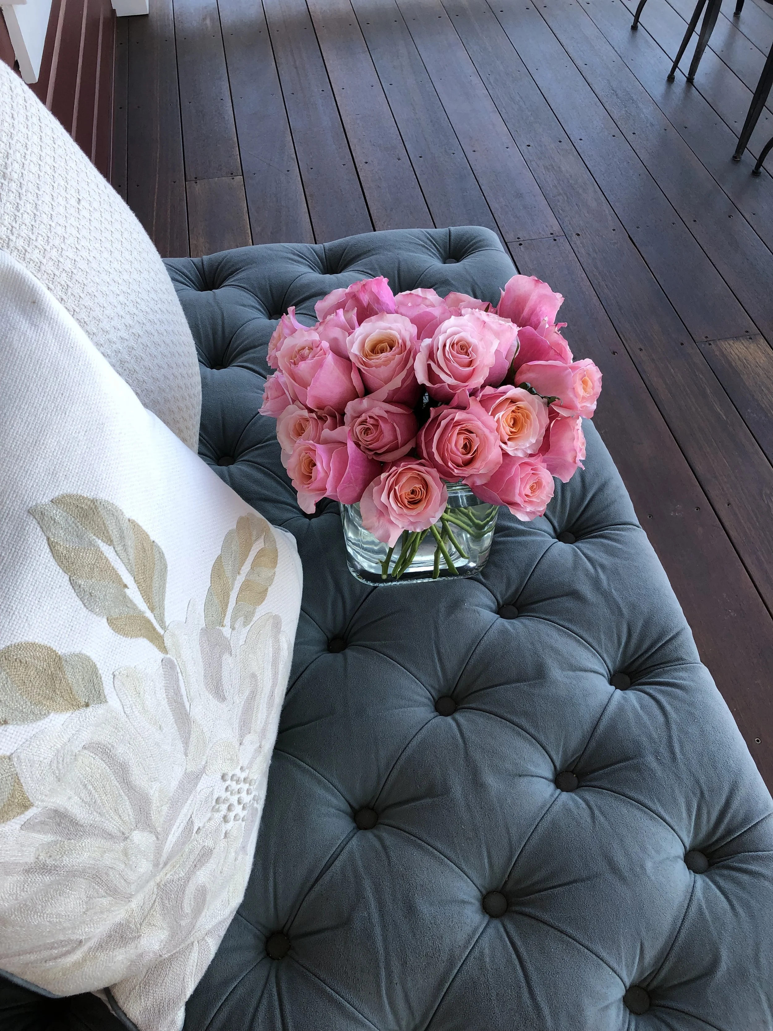 Arrangement of pink roses in clear, glass vase on tufted settee on front porch. (Floral design and photo credit: Melissa Mitchell-Hooge)