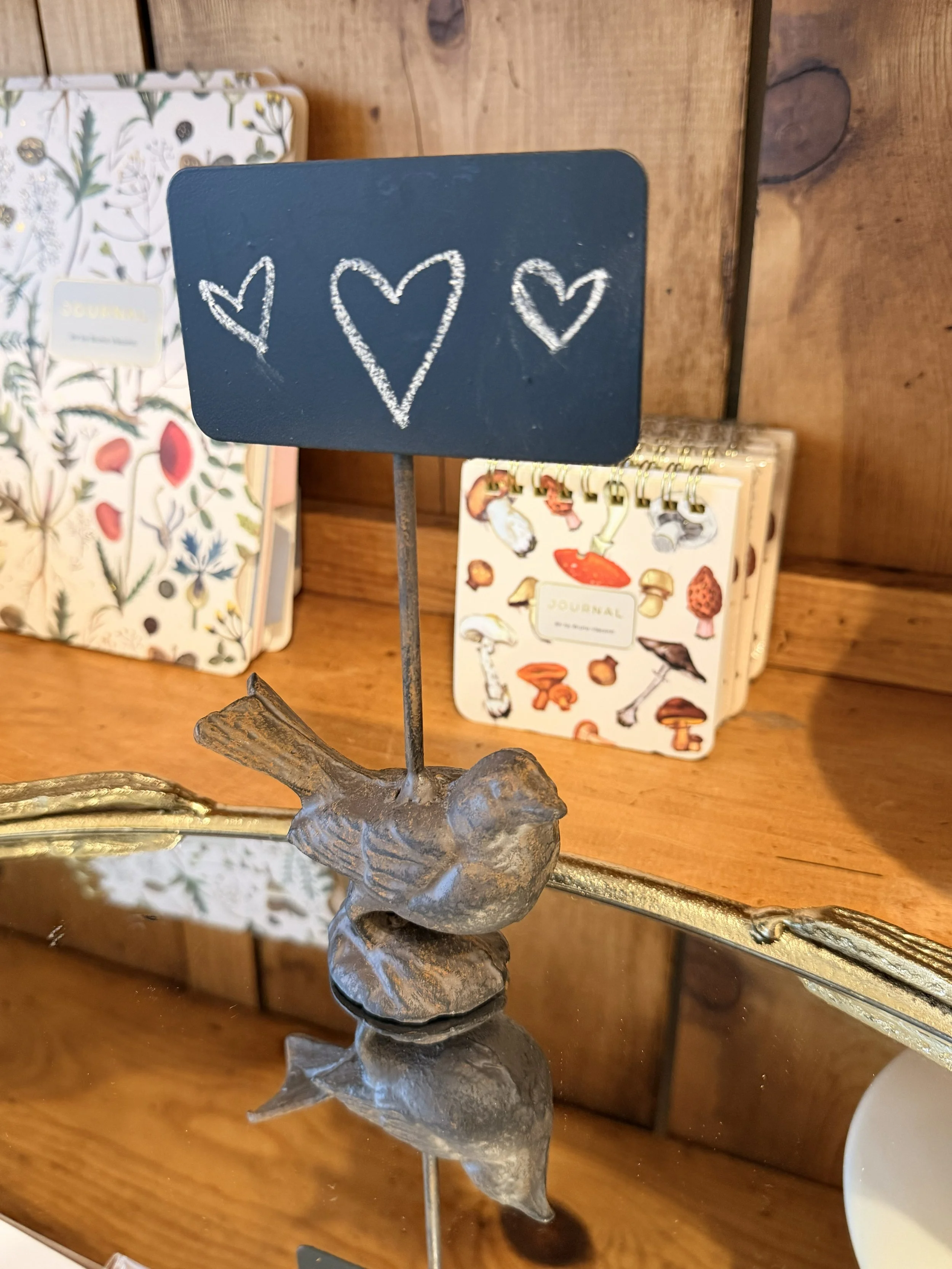 Our sweet little bird chalkboard sign with hearts graces this mirror display. Greens and Flowers Art Journals by BV by Bruno Visconti (left) and Mushrooms Pocket Art Journals also by BV by Bruno Visconti (right) on display in the background at Bloomi