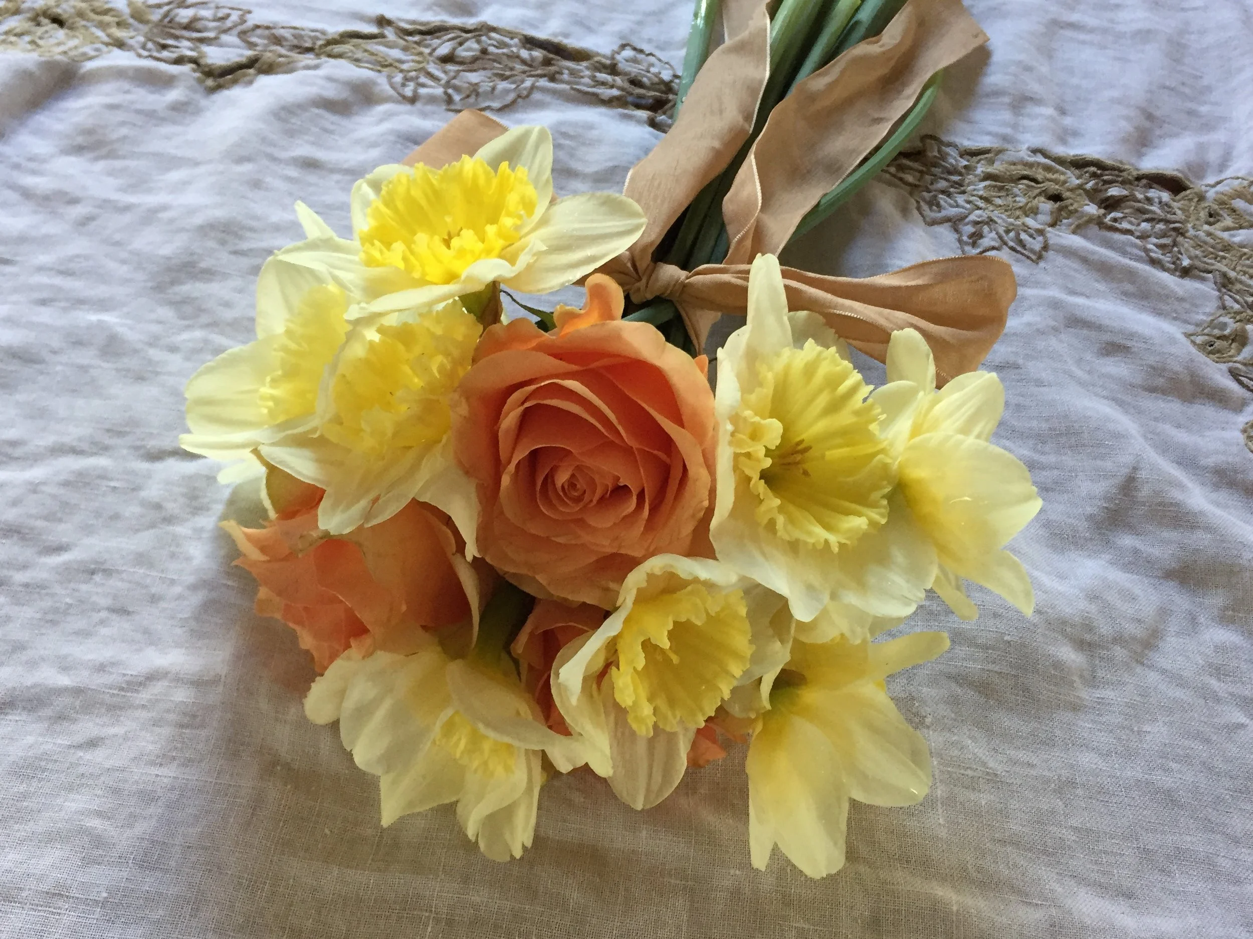 A posy of golden yellow daffodils with orange roses tied with a tan ribbon. (Floral design and photo credit: Melissa Mitchell-Hooge)