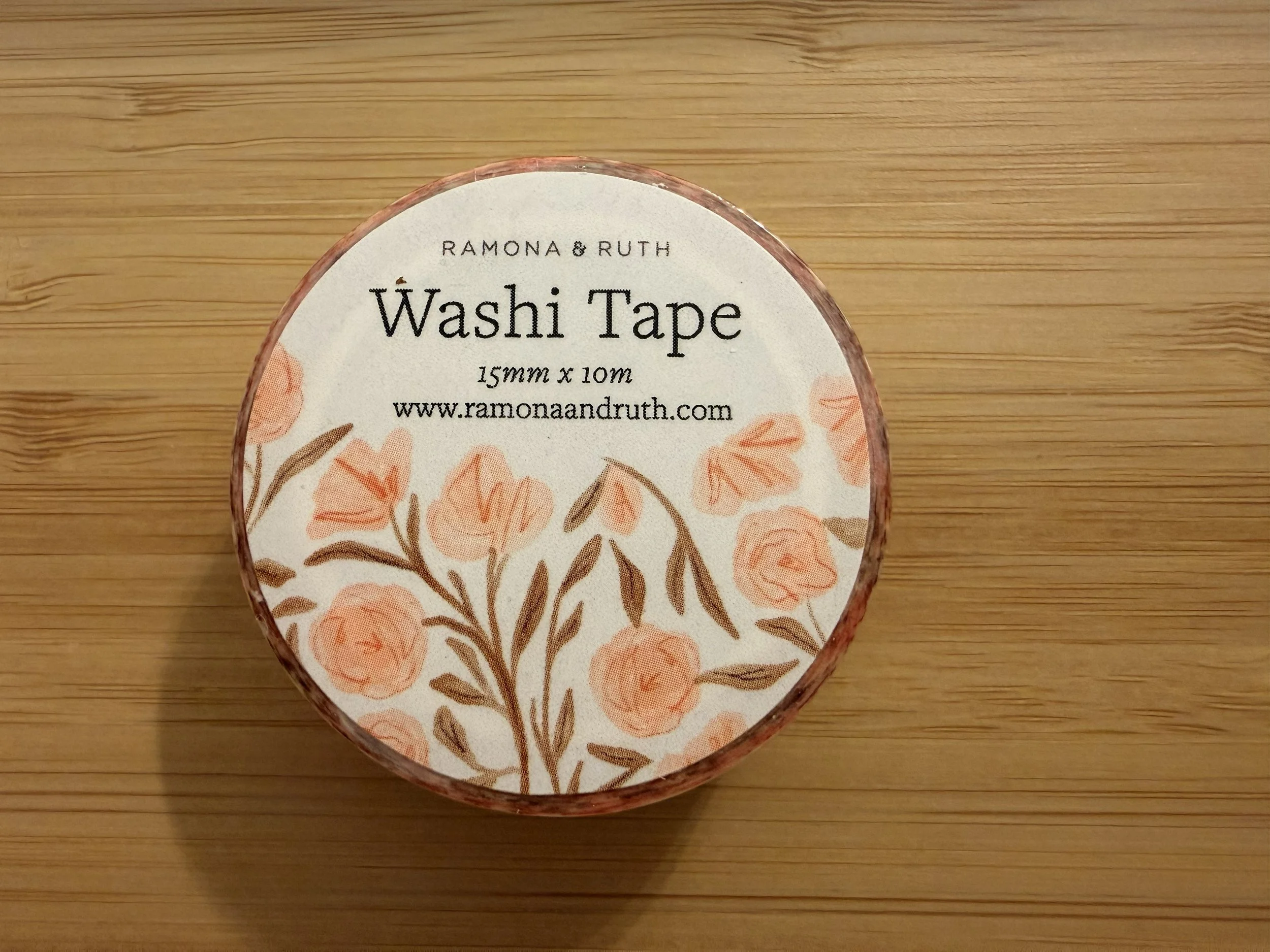 One roll of Ramona & Ruth's Pink Floral Washi tape laying flat on bamboo