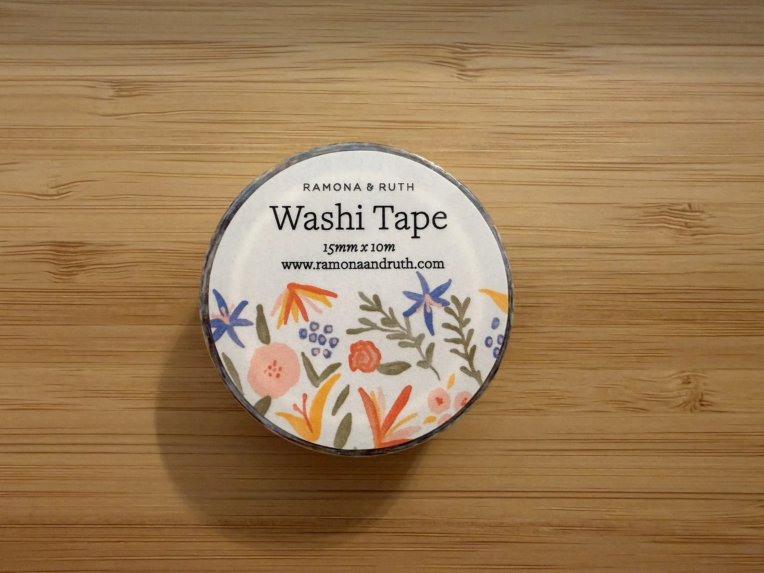 Front view of a roll of Ramona & Ruth's Spicy Floral Washi Tape laying flat on wood countertop