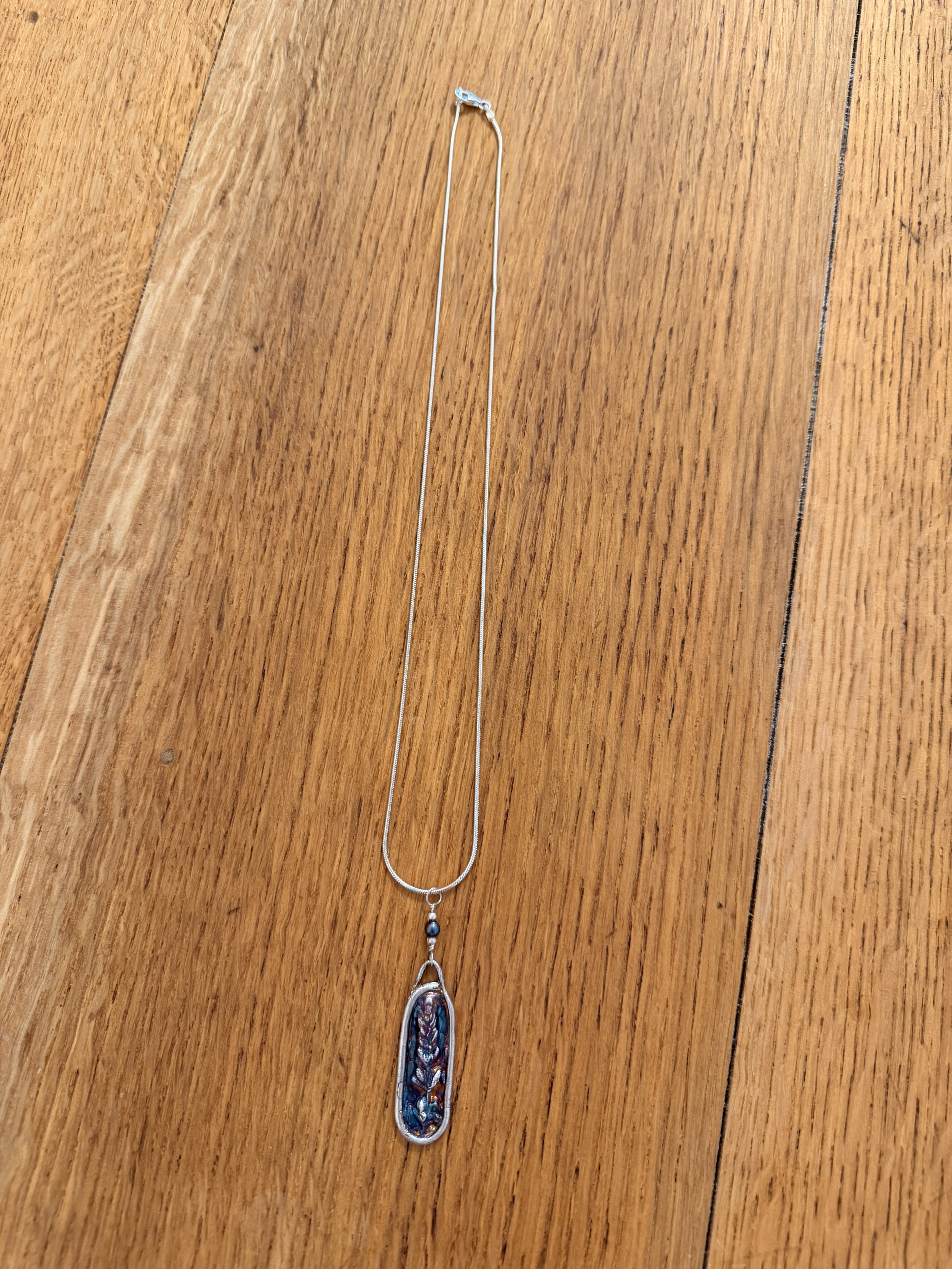 Tucci'Z Designs fine silver pendant with lavender design on sterling silver necklace on wood countertop at Bloomie's Boutique
