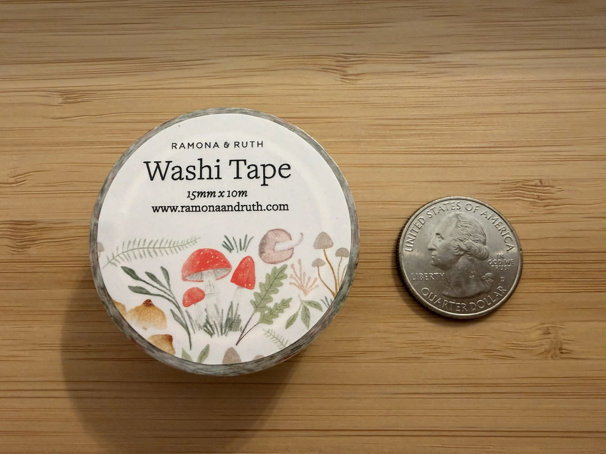 One roll of Ramona & Ruth's Mushroom Forest Washi Tape laying flat with quarter on bamboo