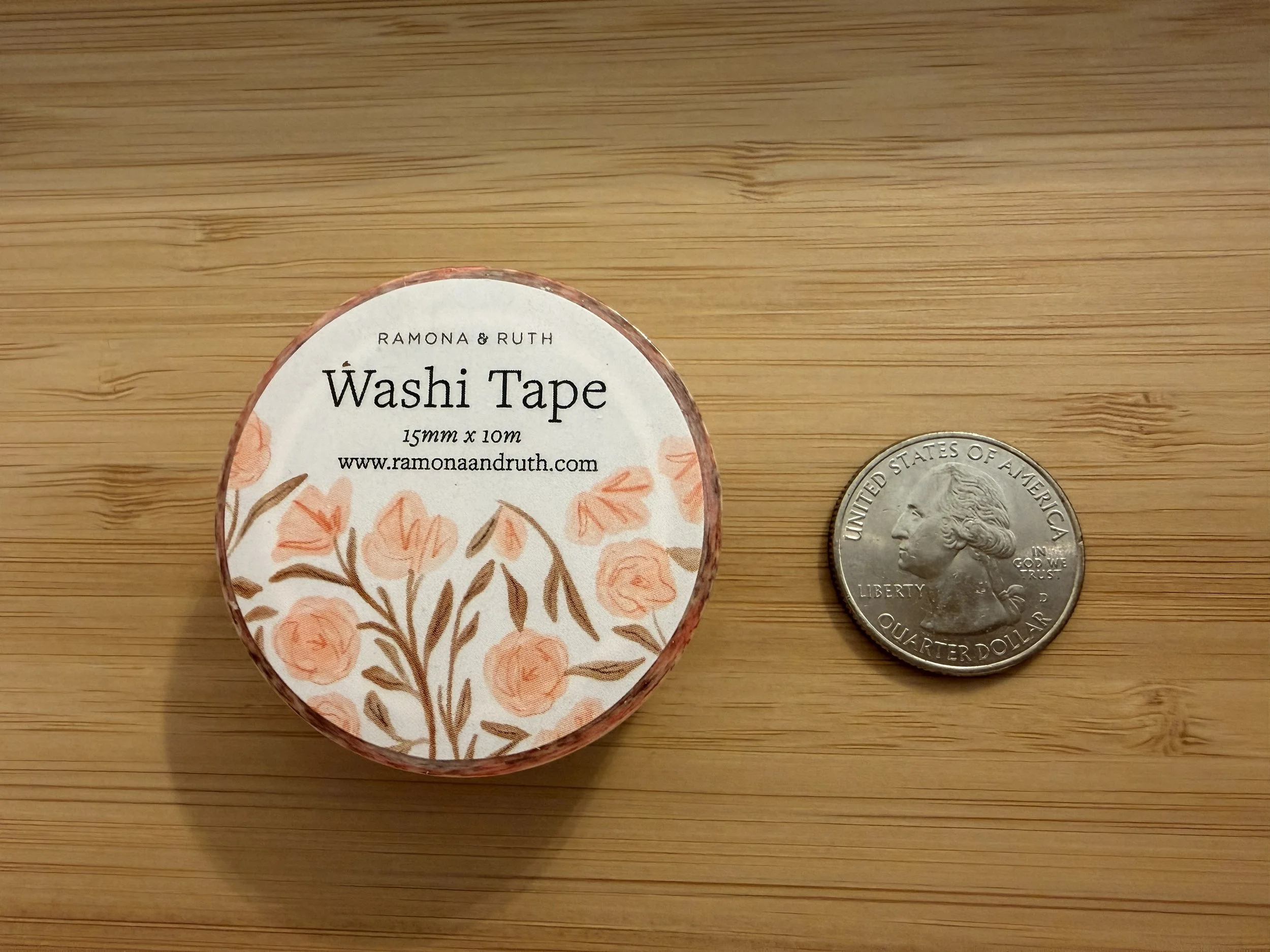 One roll of Ramona & Ruth's Pink Flowers Washi Tape laying flat with quarter on bamboo