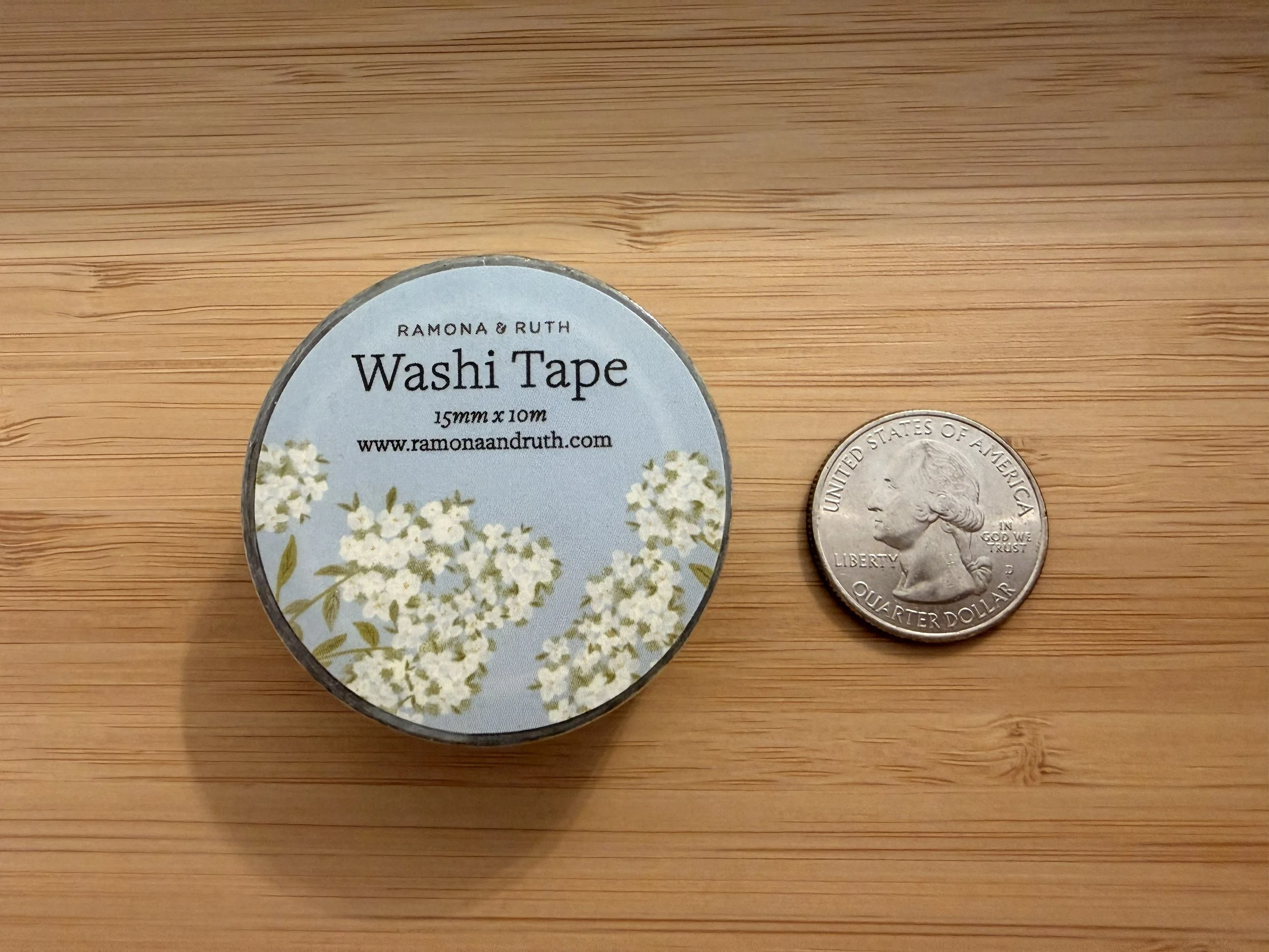 One roll of Ramona & Ruth's Hydrangea Washi Tape laying flat with quarter on bamboo