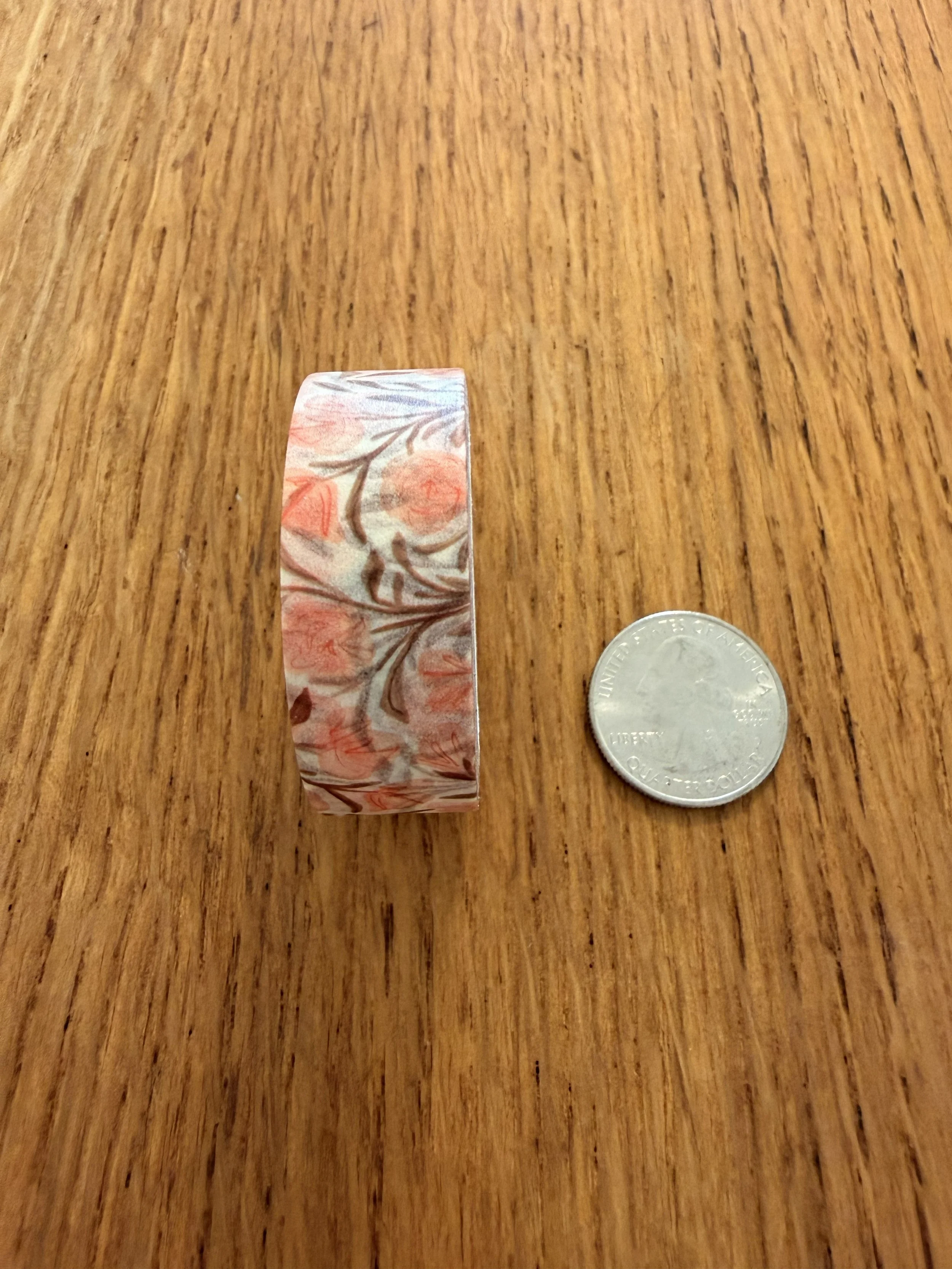 One roll of Ramona & Ruth's Pink Floral Washi Tape on edge with quarter on wood countertop
