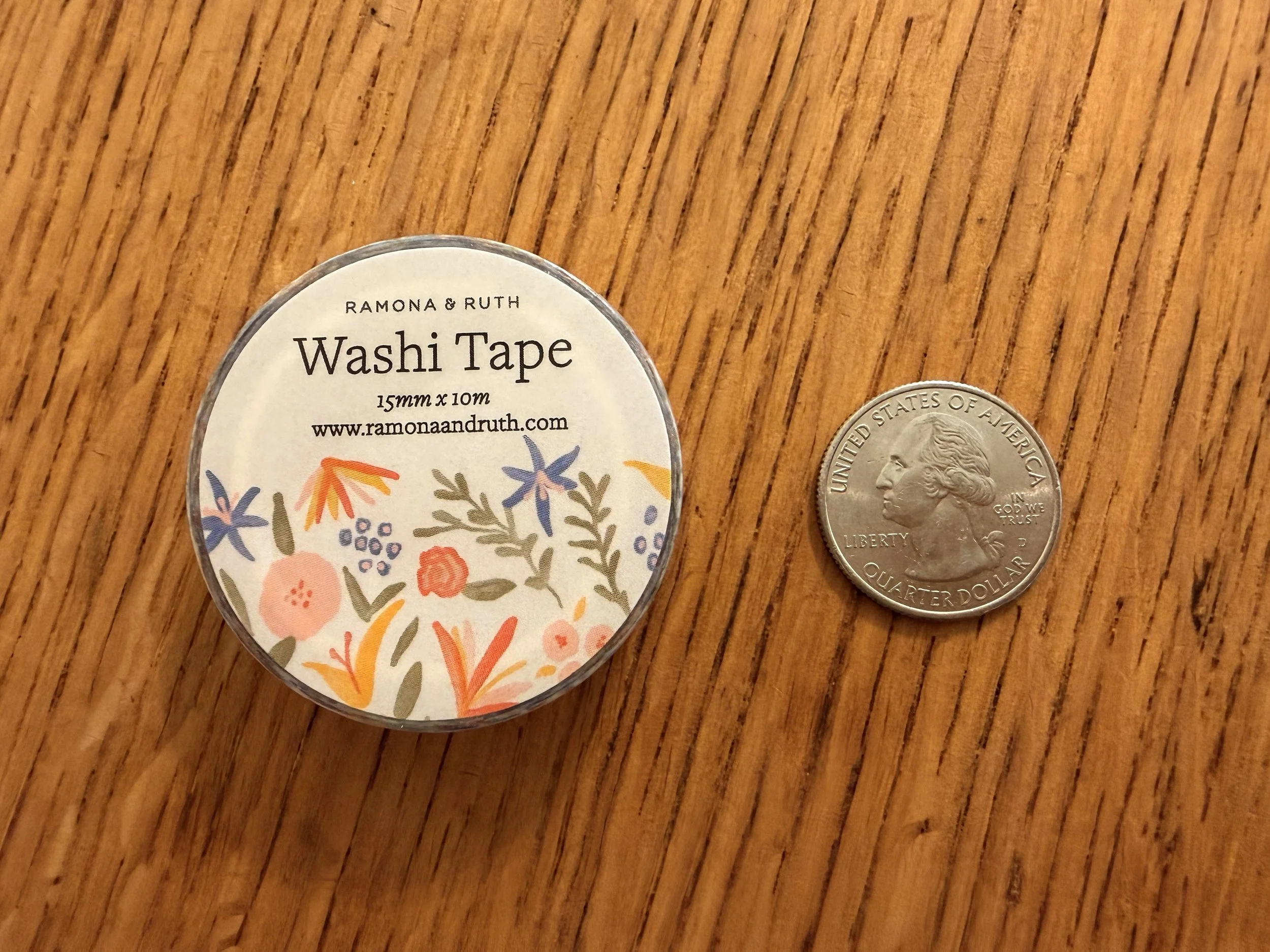 One roll of Ramona & Ruth's Spicy Floral Washi Tape laying flat on wood countertop with quarter