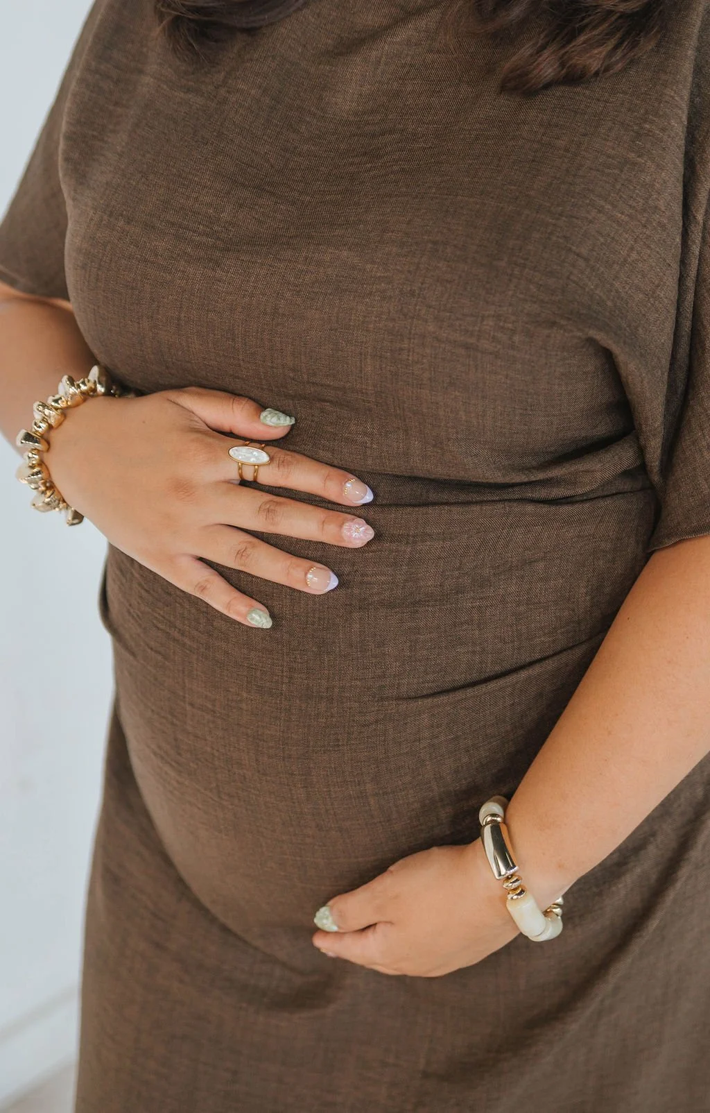 An expectant mother wheres a brown woven dress and holds her pregnant belly at a pre-natal support class.