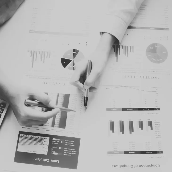 Hands analyzing financial charts and graphs on paper, with pens, during a business or finance meeting.