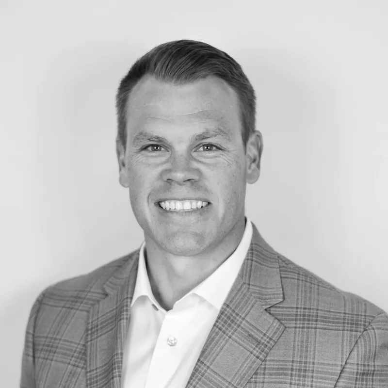 Black and white professional headshot of a smiling man wearing a suit jacket and white shirt.