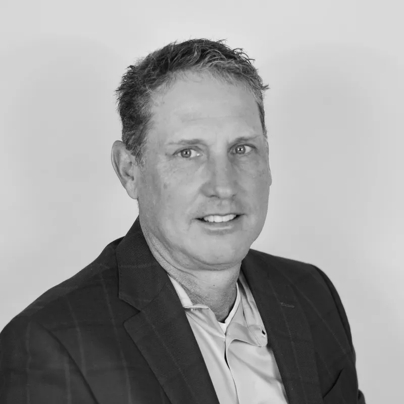 Black and white portrait of a man wearing a checked blazer and a collared shirt, smiling at the camera.
