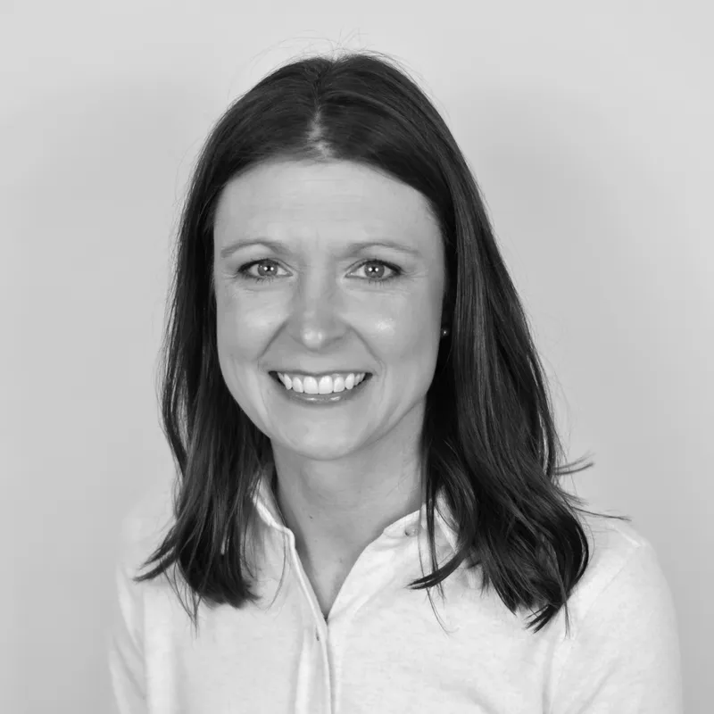 Black and white headshot of a smiling woman with shoulder-length hair, wearing a collared shirt, against a plain background.