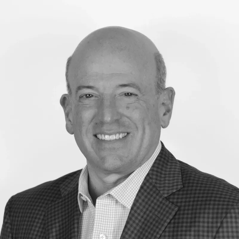 Black and white professional headshot of a smiling bald man in a checkered blazer and collared shirt.