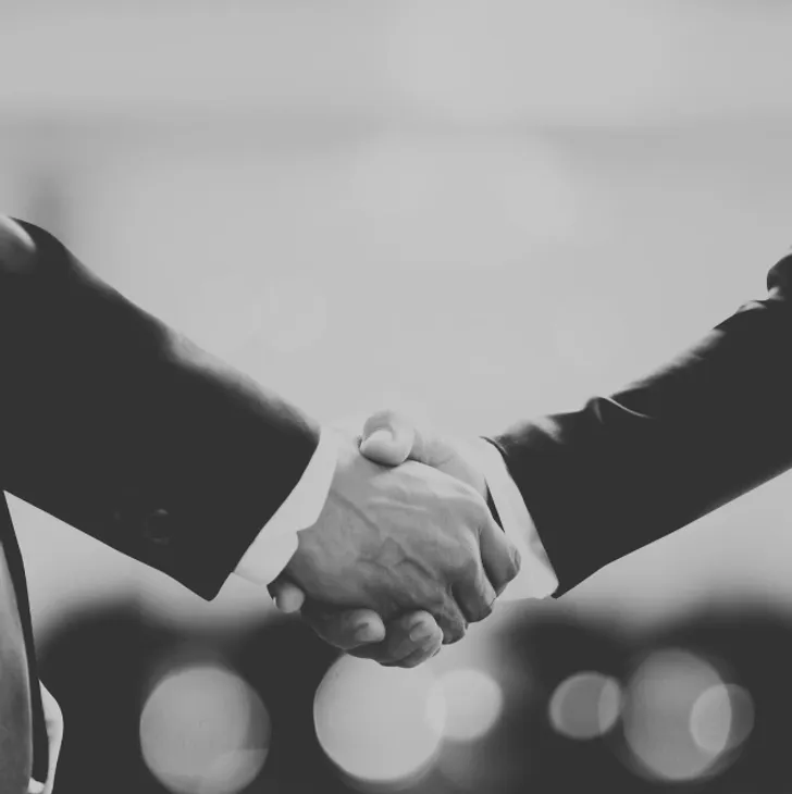 A black-and-white photo of two people shaking hands, wearing suits.