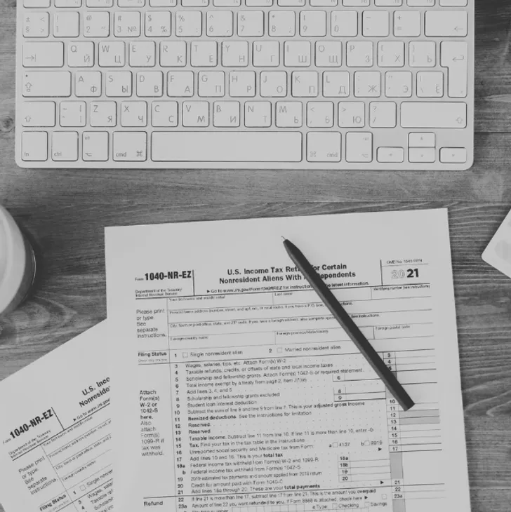 A computer keyboard, a pen on a U.S. income tax form, and a cup on a wooden desk.