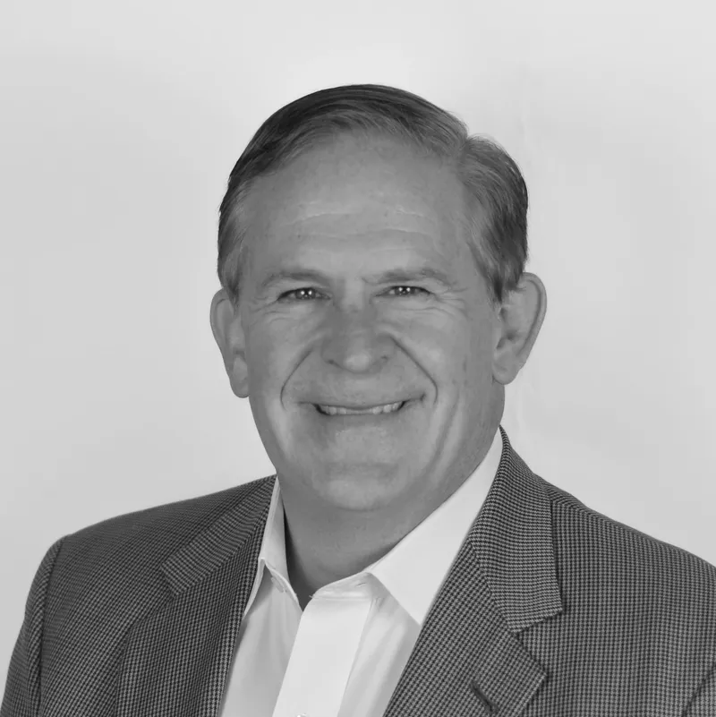 Black and white professional headshot of a smiling middle-aged man with short hair, wearing a suit jacket and white collared shirt, against a plain background.