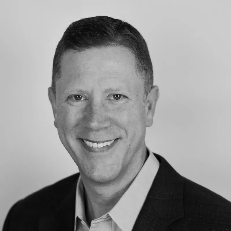 Black and white professional portrait of a smiling man in a suit and collared shirt.