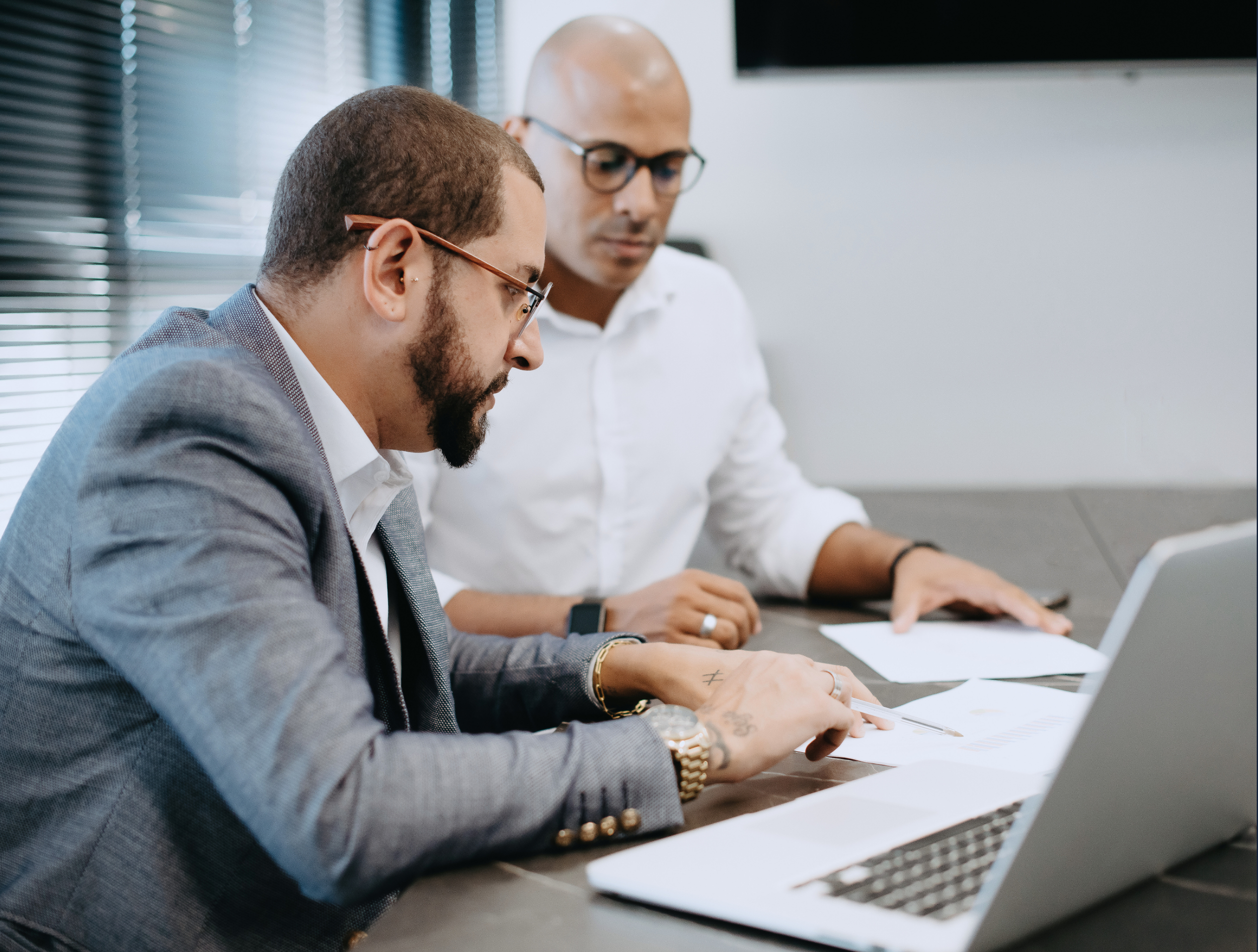 Two men working together in an office, looking at documents and a laptop on a desk.