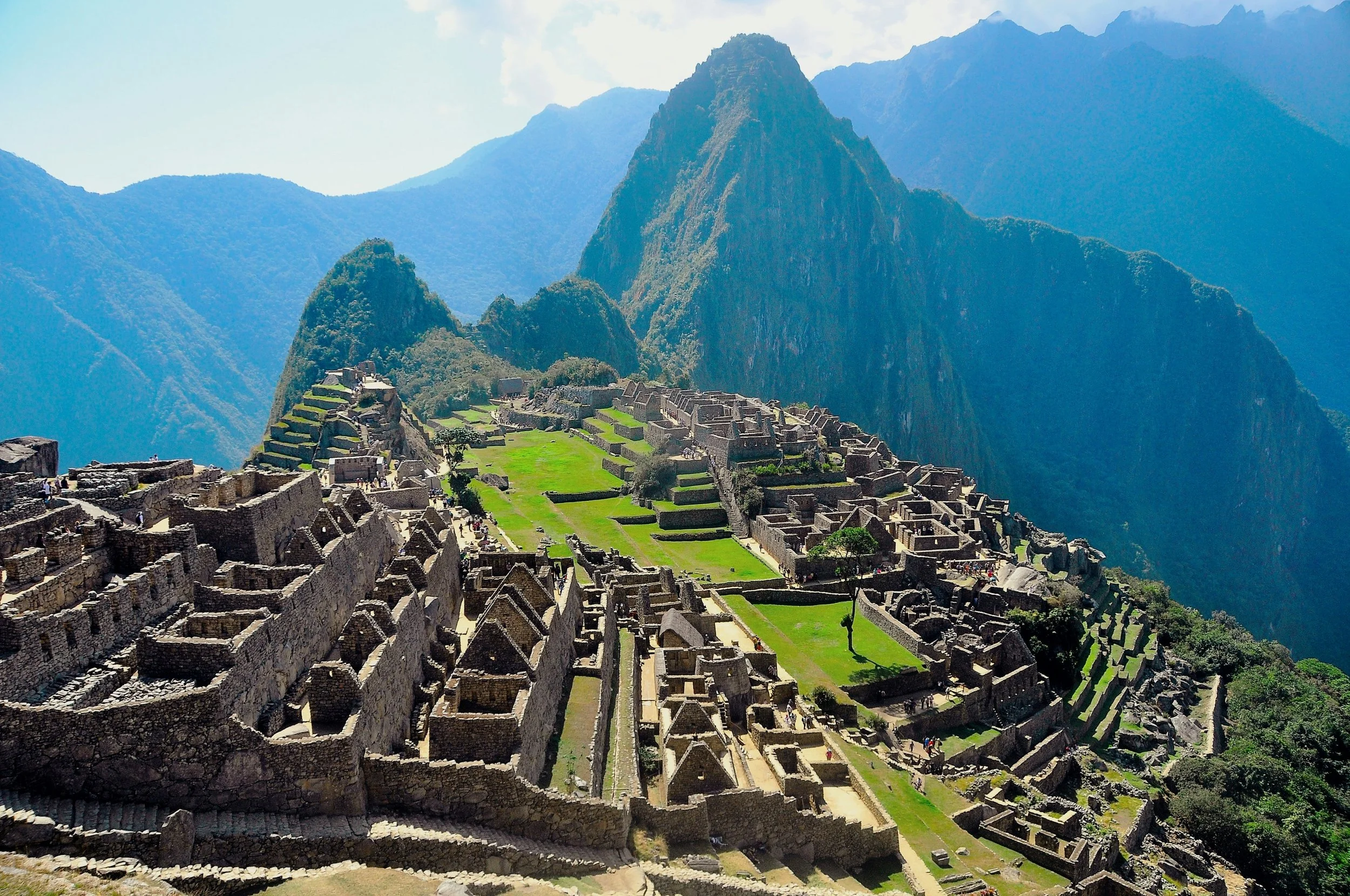 Ancient ruins of Machu Picchu with stone terraces and buildings on a mountain in Peru, surrounded by lush green forests and steep peaks under a cloudy sky.