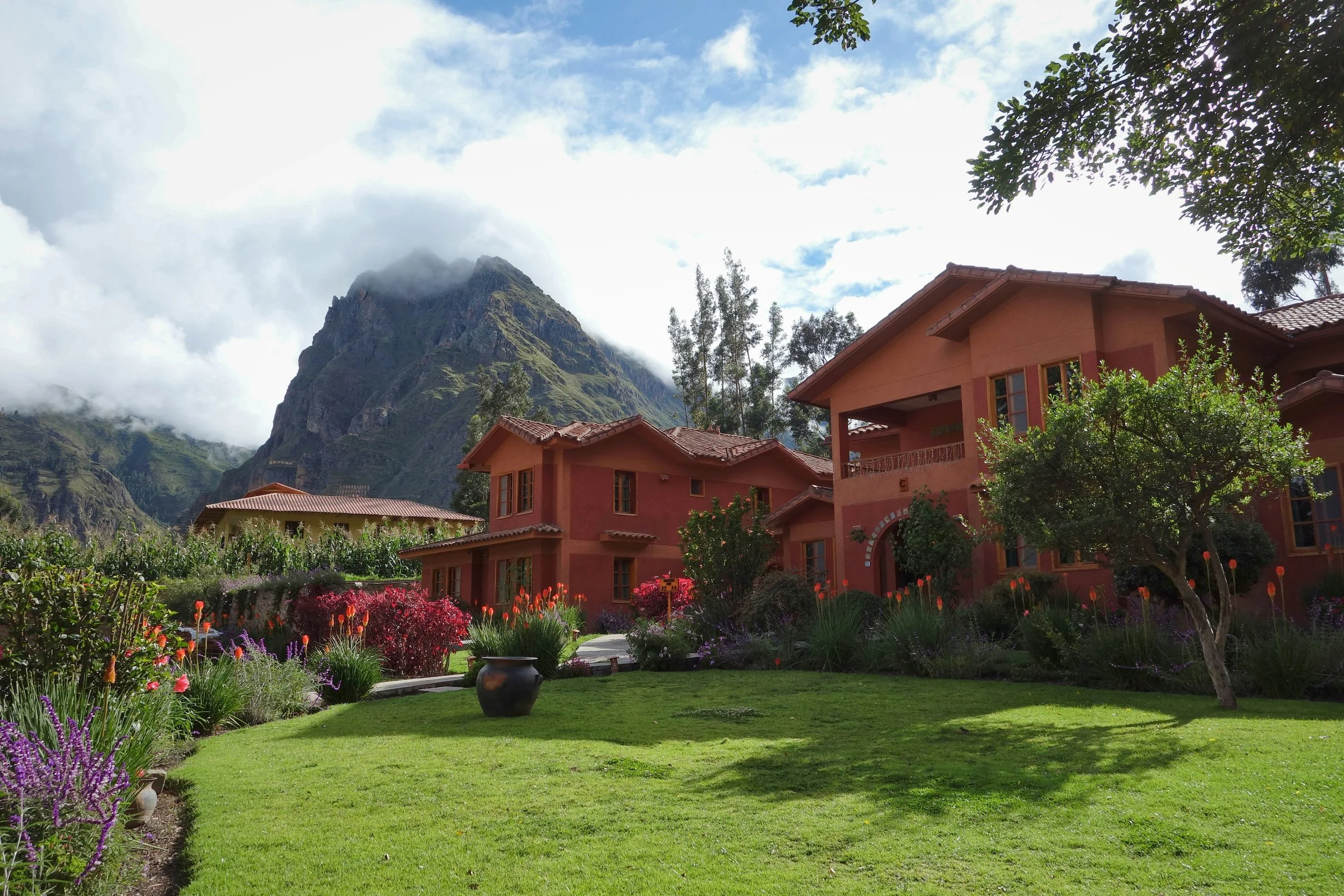 A house with a garden in front of a mountain with clouds