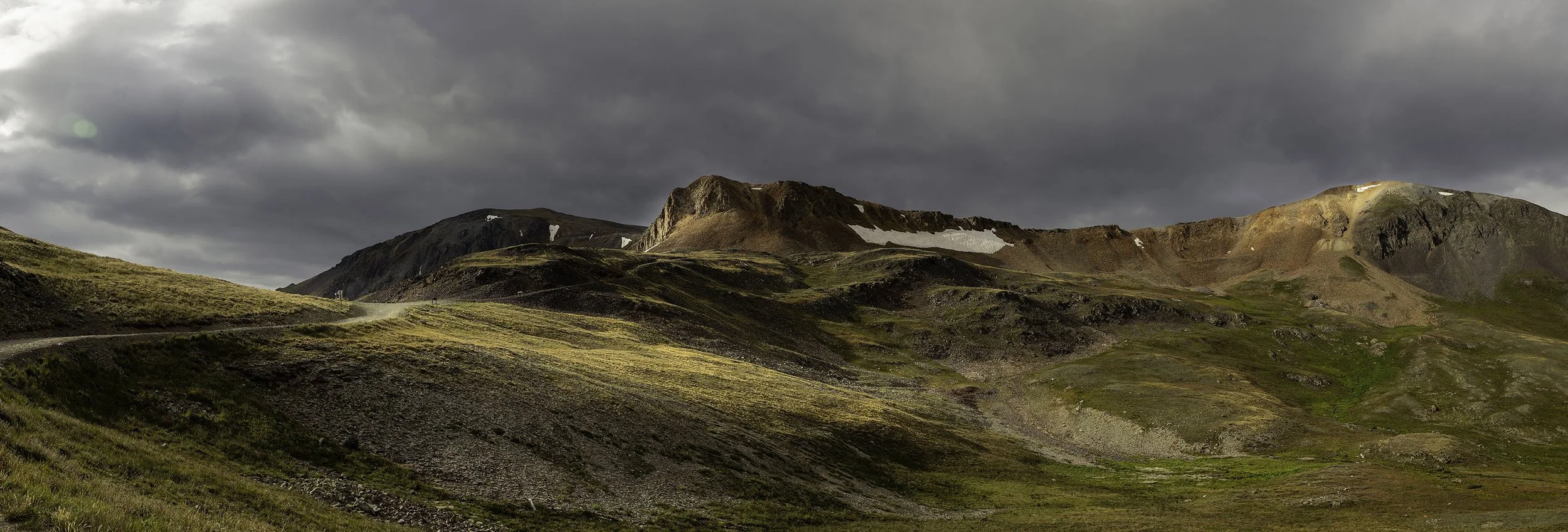 Mountain landscape with grassy rolling hills, rocky peaks, and dark cloudy sky