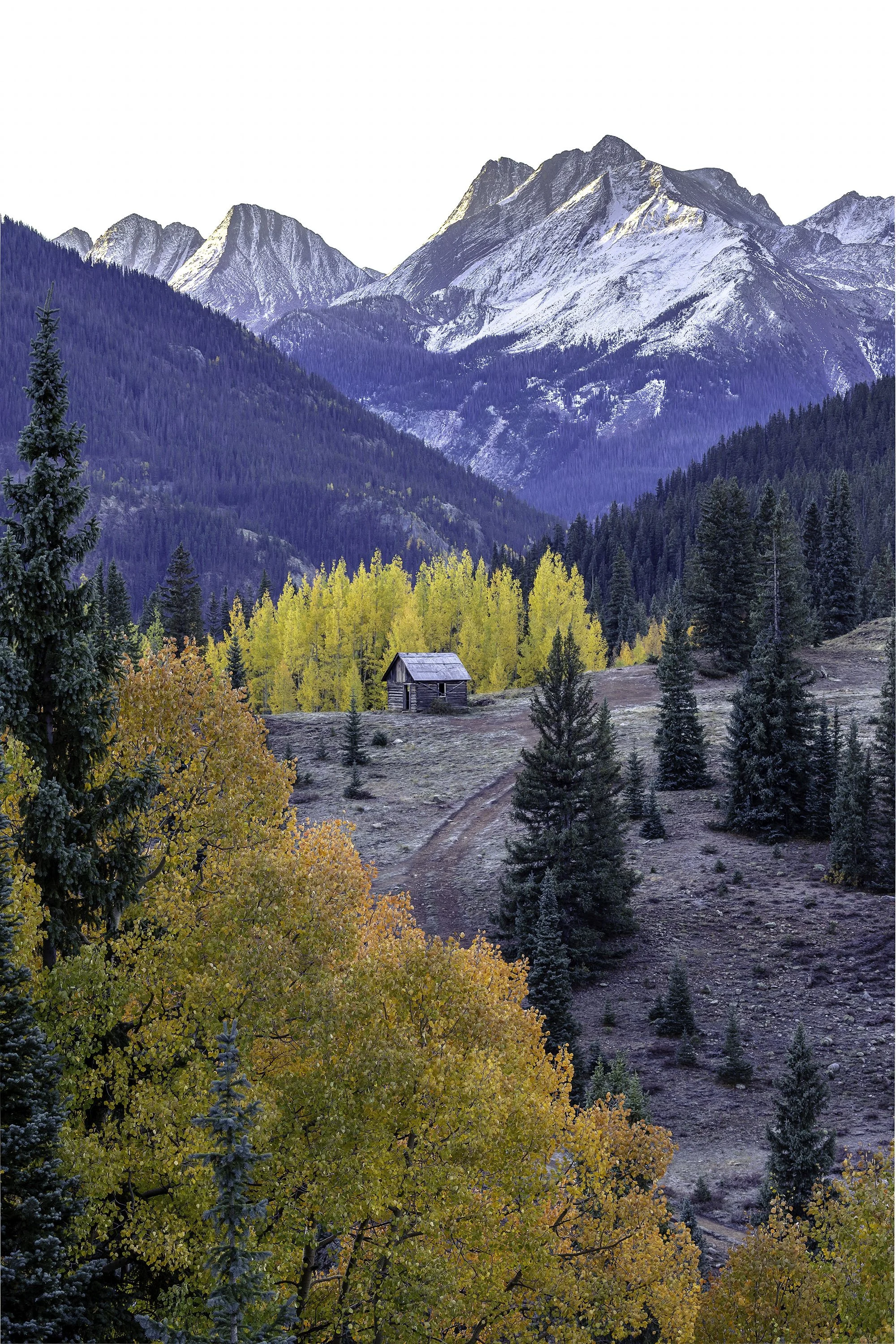 A mountain landscape with snow-capped peaks, dense evergreen forests, and colorful autumn trees surrounding a small wooden cabin on a hillside.