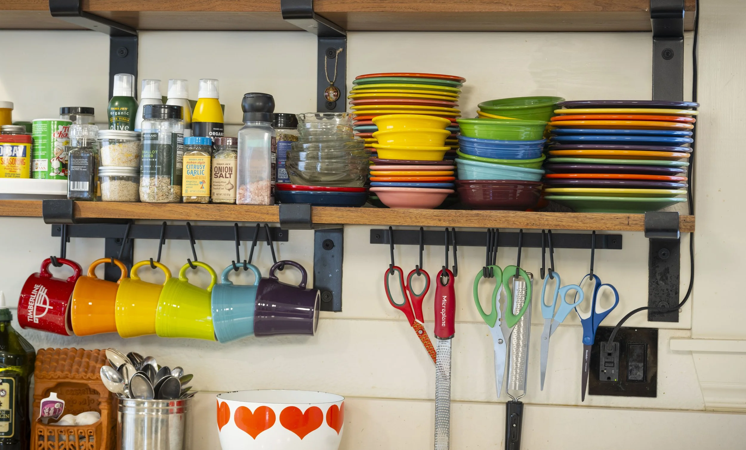 Kitchen shelf with colorful cups, plates, and kitchen utensils such as scissors, measuring spoons, and a measuring tape.