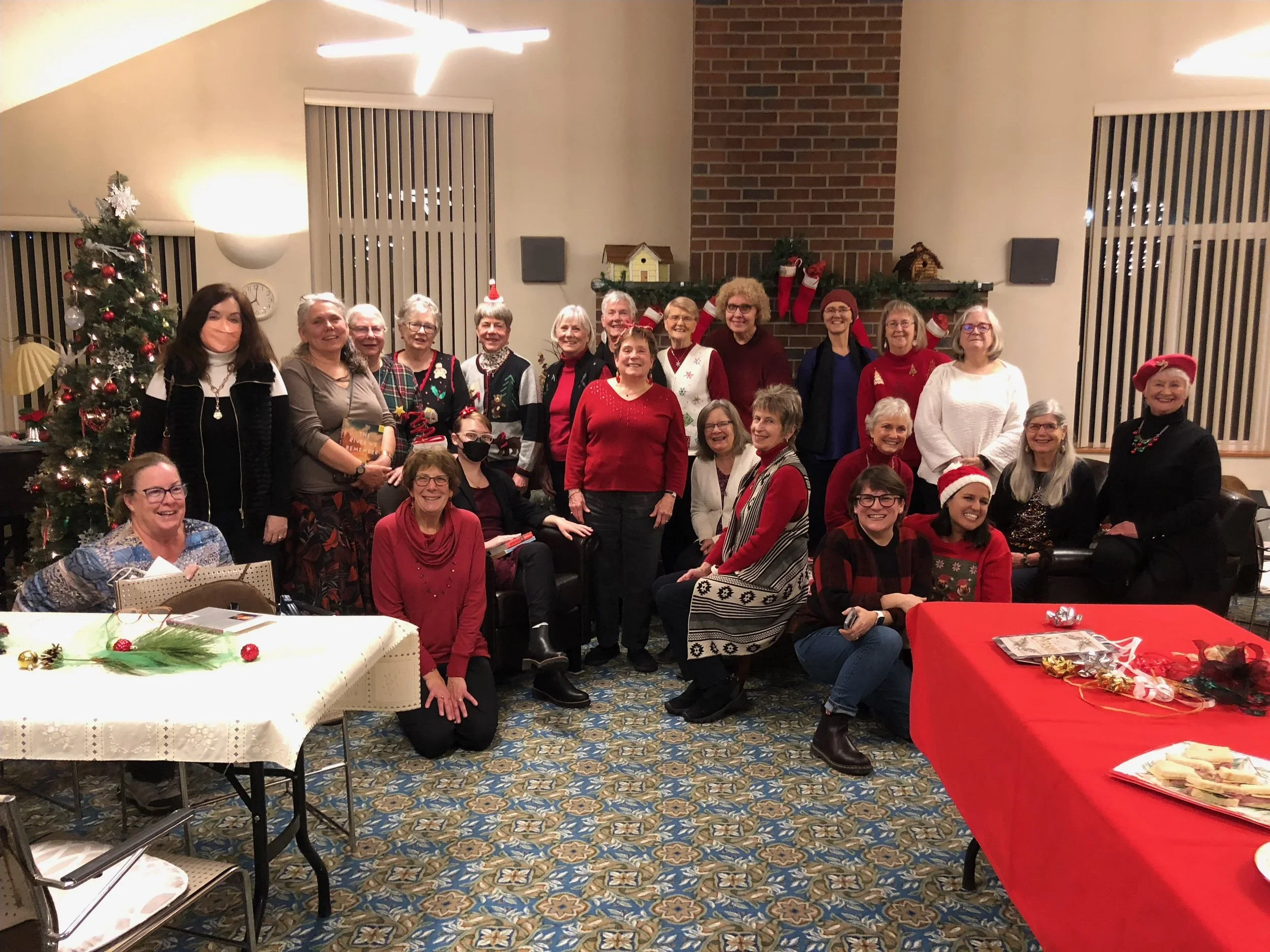 Group of women gathered at a Christmas party in a decorated room with a Christmas tree, Santa hats, and holiday decorations.
