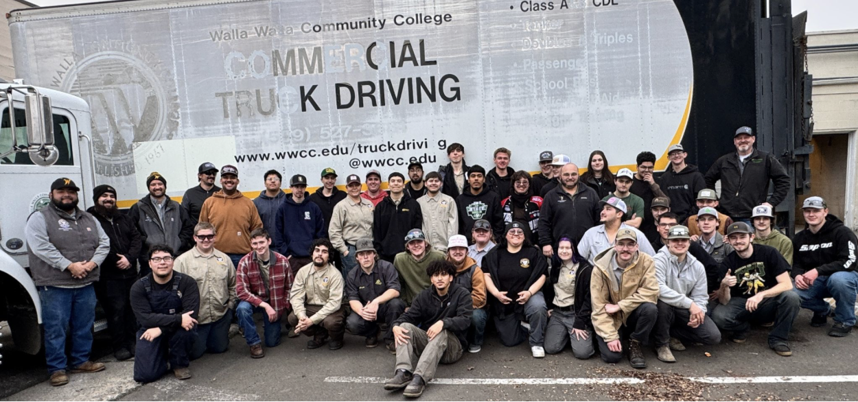 Group photo of students and instructors at a Truck Driving class at Walla Walla Community College, in front of a large truck with a banner advertising the program.