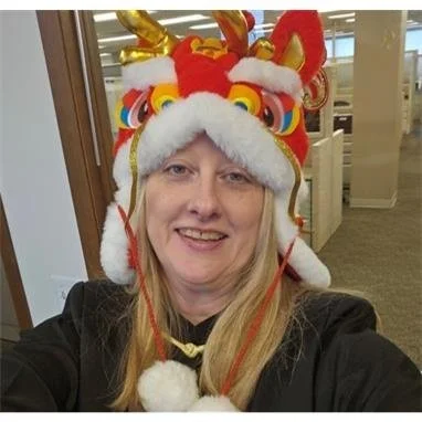 Woman wearing a colorful dragon Chinese New Year hat with red, gold, and white colors, in an indoor setting.