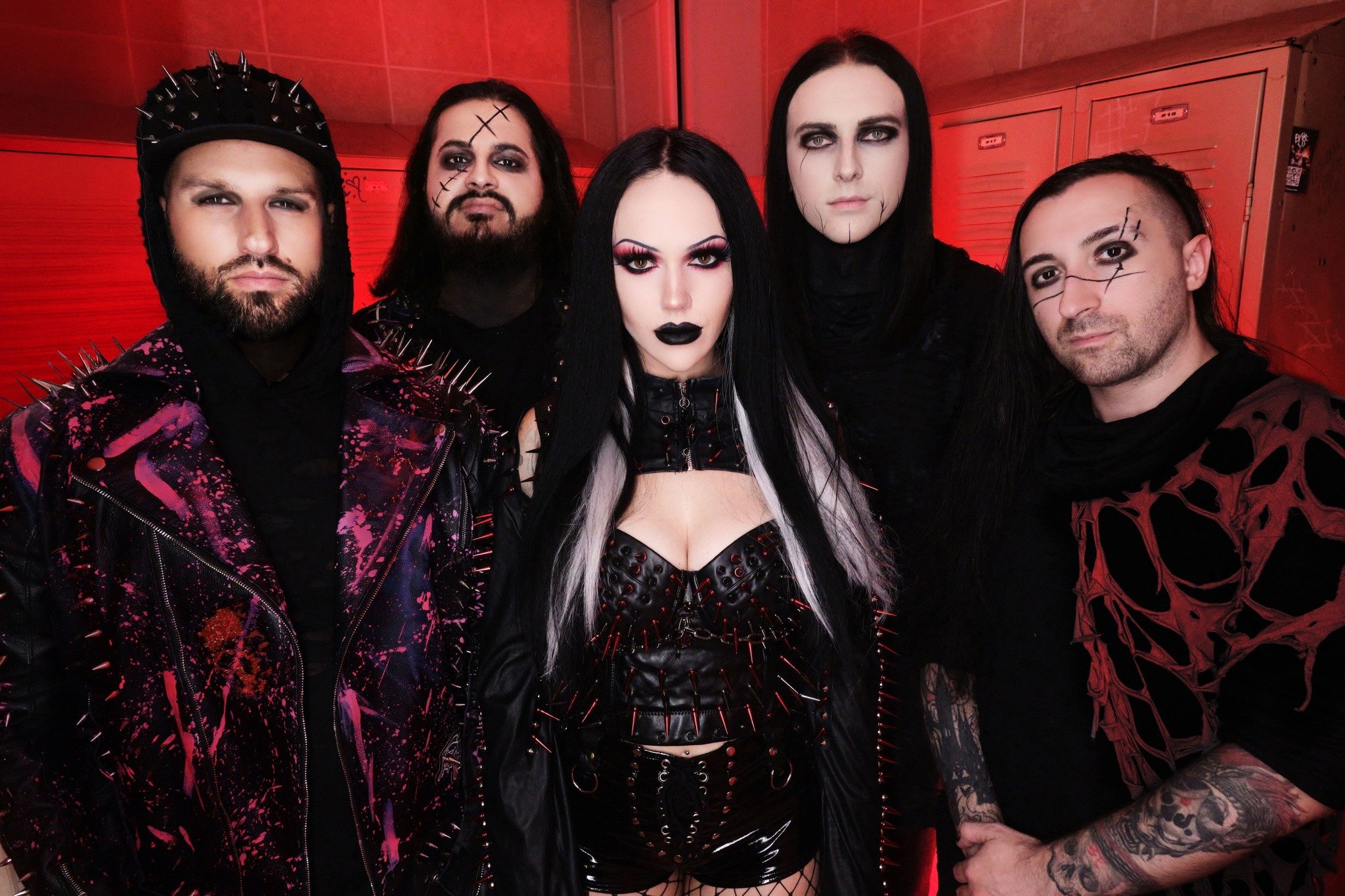 Group of five people dressed in dark, edgy, gothic fashion, posing in front of red lockers.