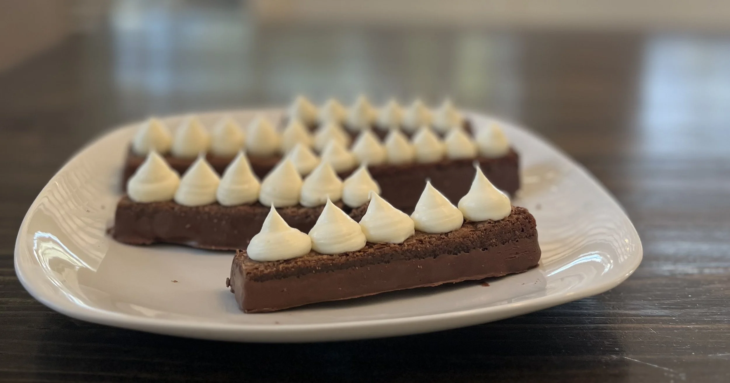 Chocolate desserts with white cream piped on top, served on a white plate on a wooden table.