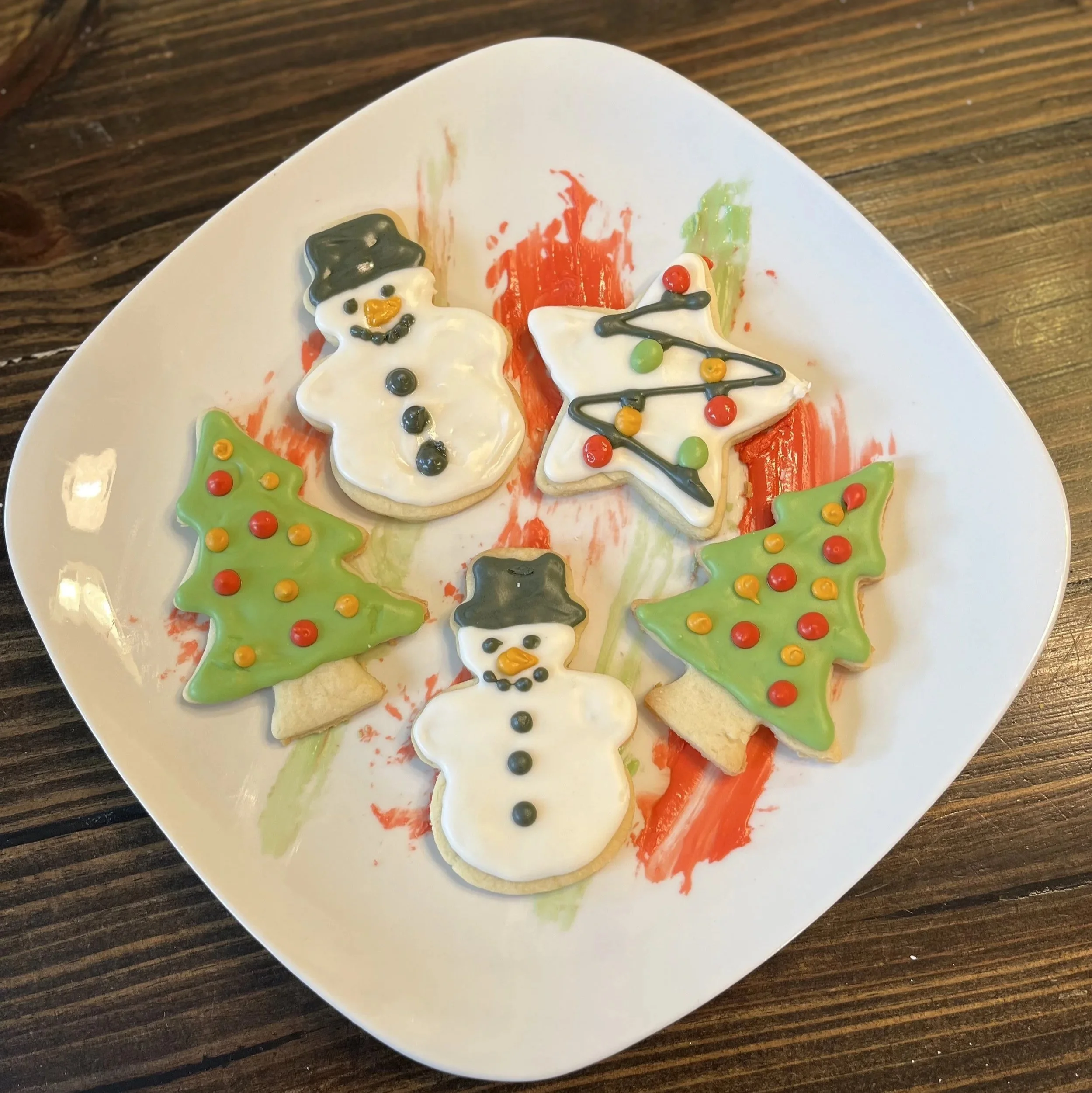 Plate of Christmas-themed sugar cookies decorated with icing and colorful candy, shaped as snowmen, Christmas trees, and stars.