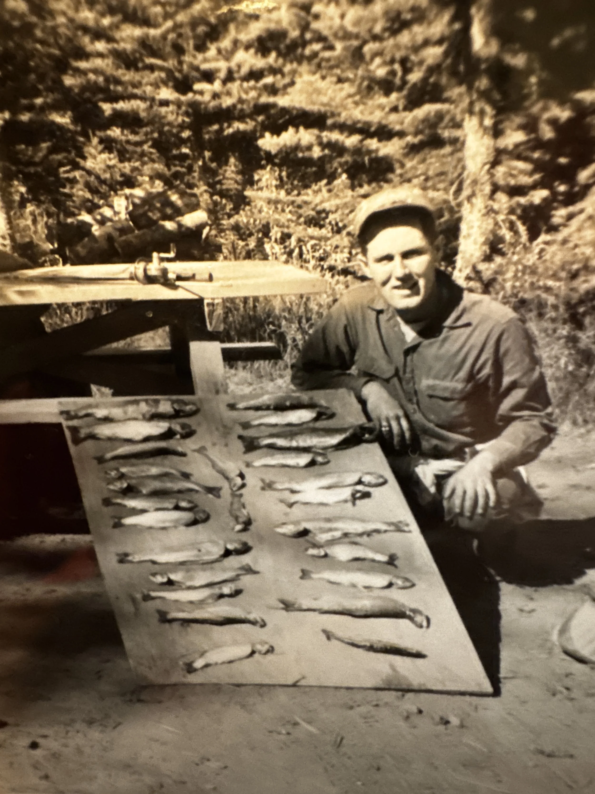 A smiling man in military uniform squatting next to a table with a large sheet displaying fish sketches.