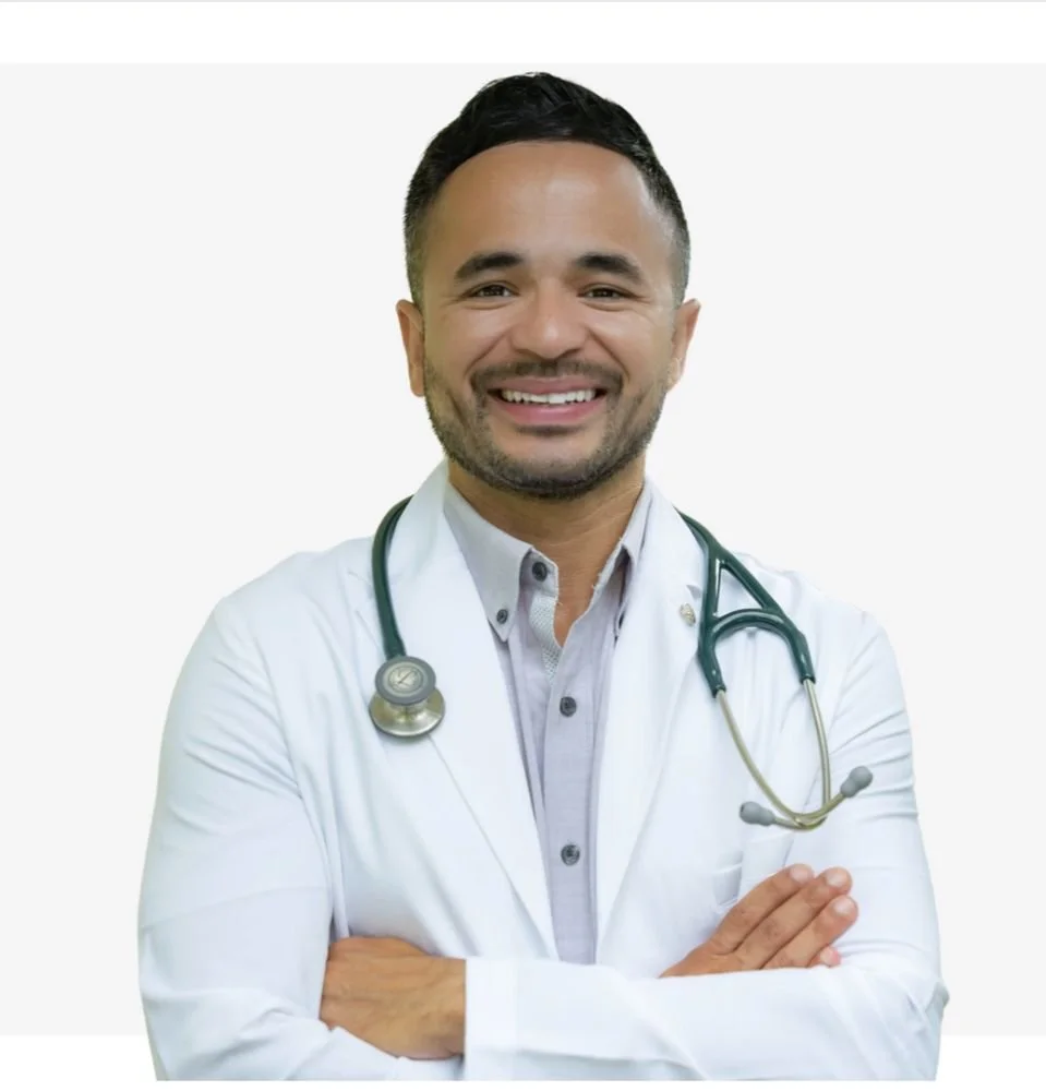 A smiling male doctor with a stethoscope around his neck, standing with arms crossed, wearing a white lab coat.
