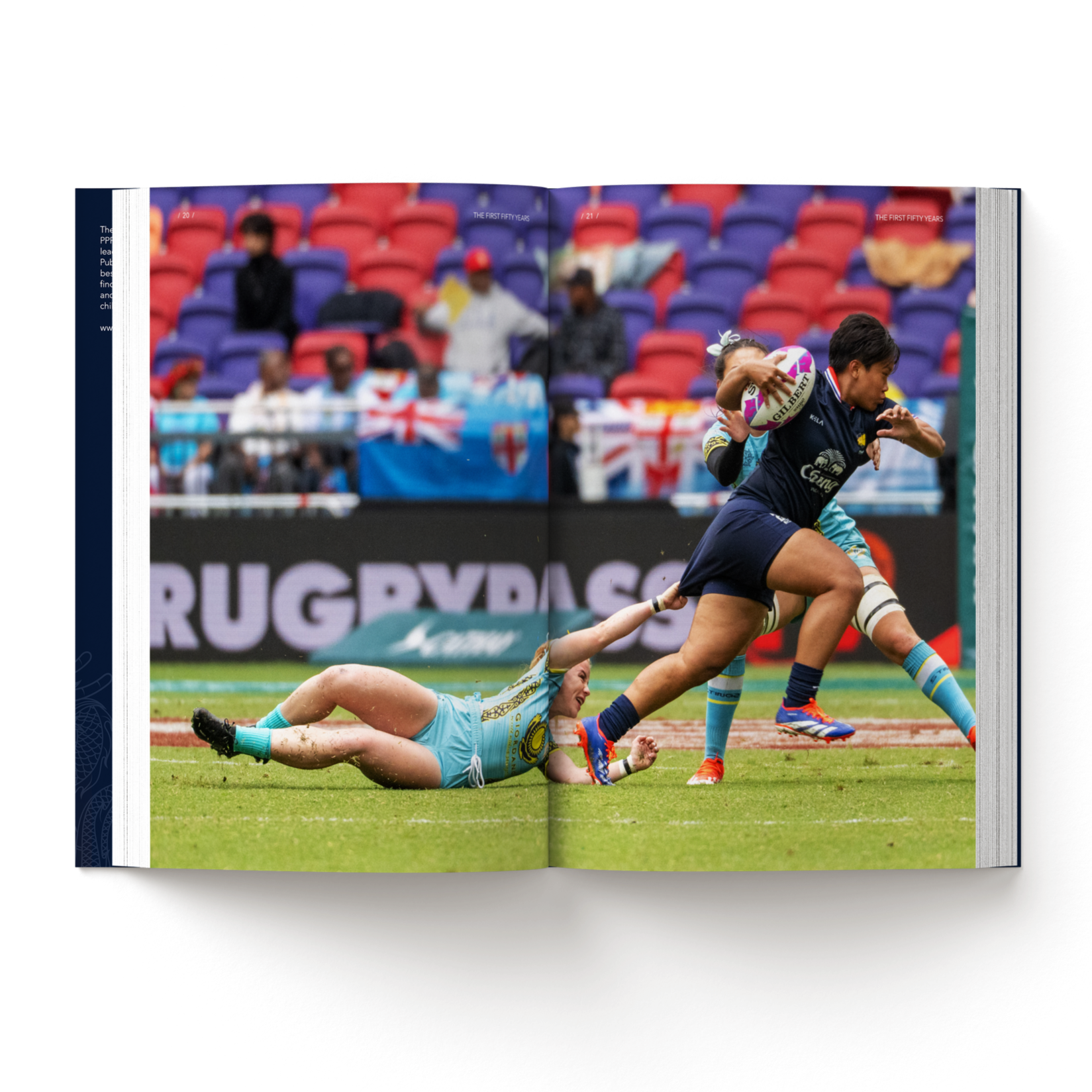 Women rugby player running with ball as another player dives to tackle on the ground during match with spectators watching. Image from mock-up of The First Fifty Years.