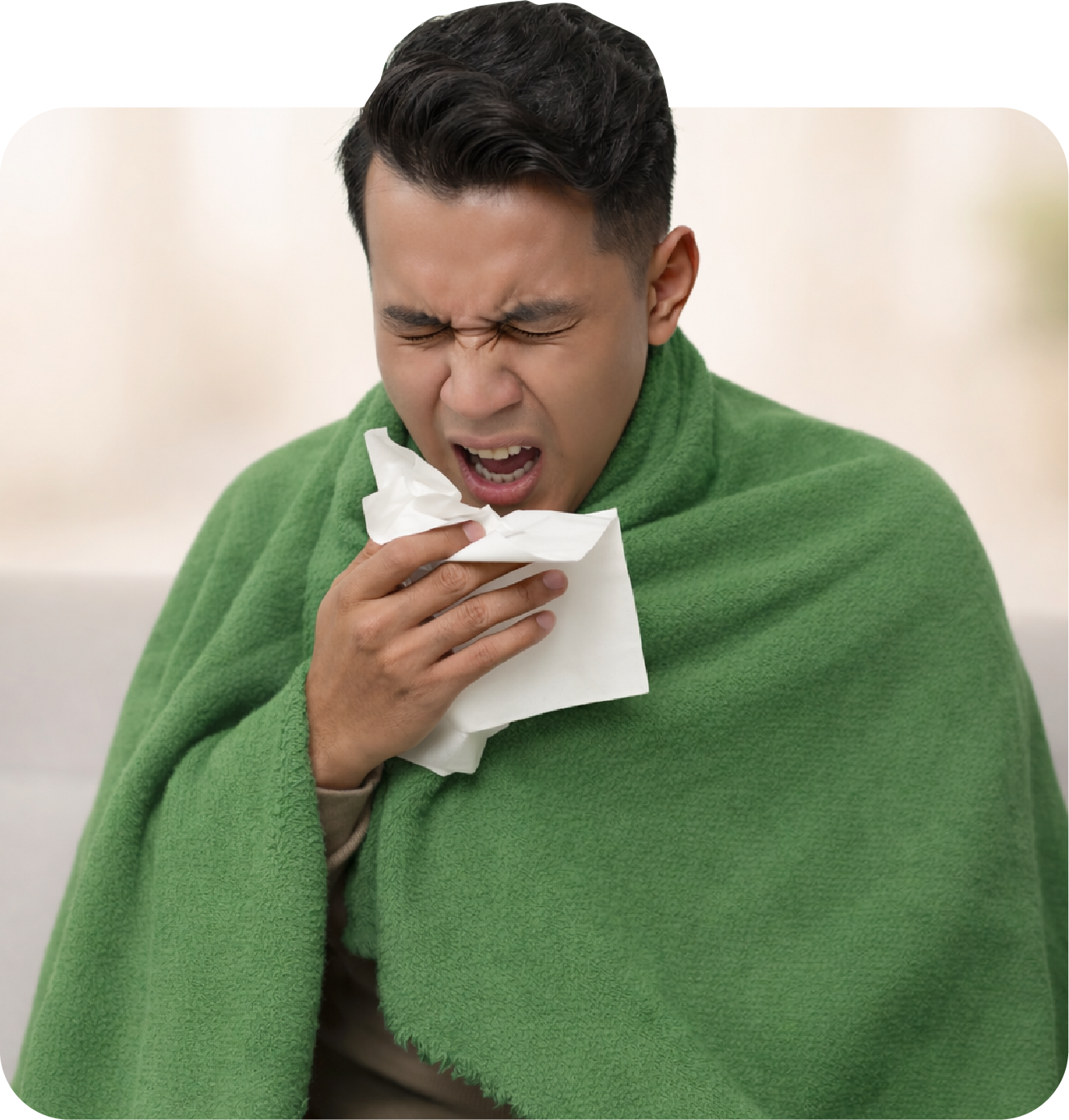 A man dressed in a green blanket appears to be coughing or sneezing into a tissue, holding it with one hand.