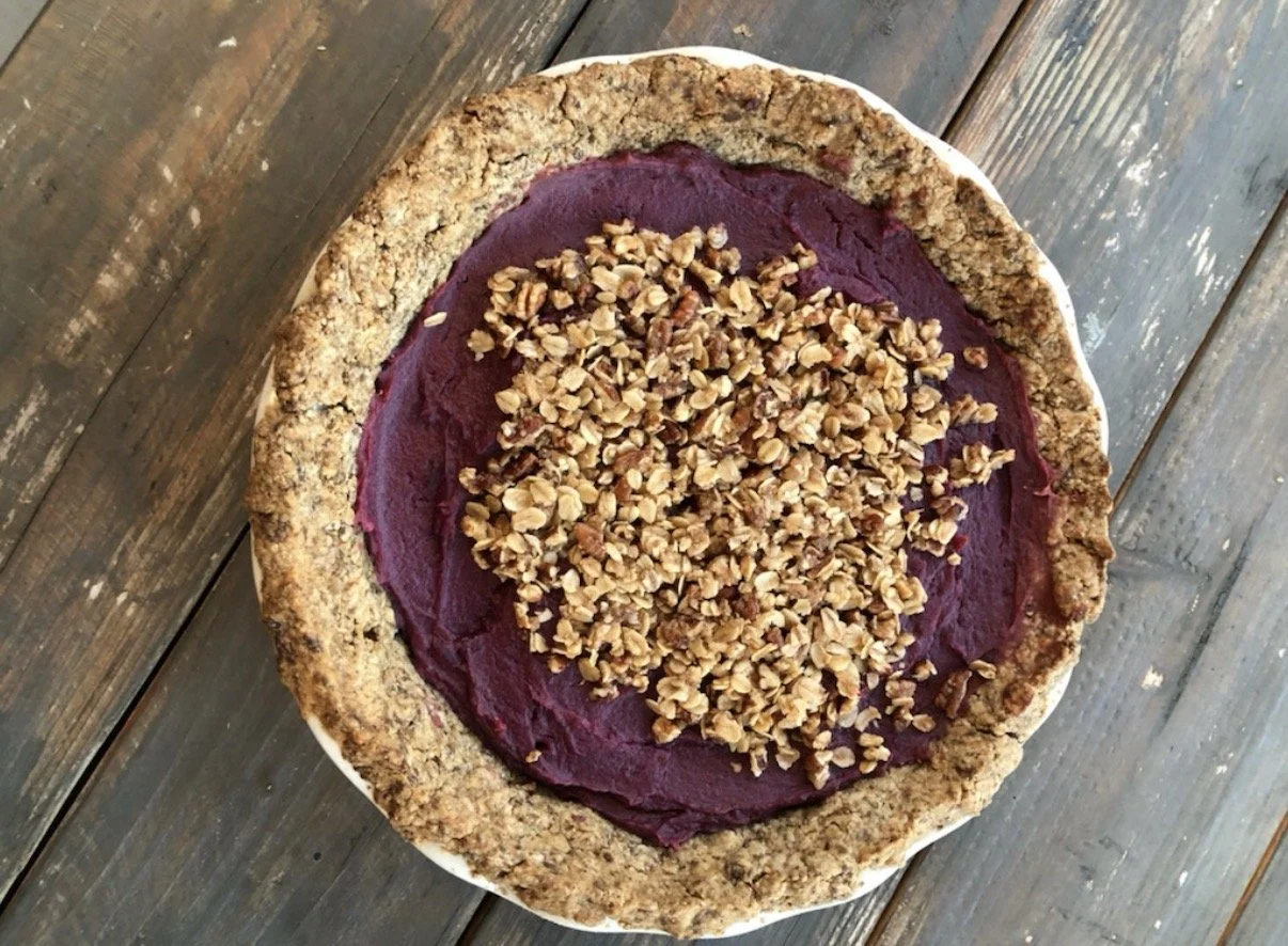 A purple sweet potatoe pie with a crumbly crust, on a wooden surface.