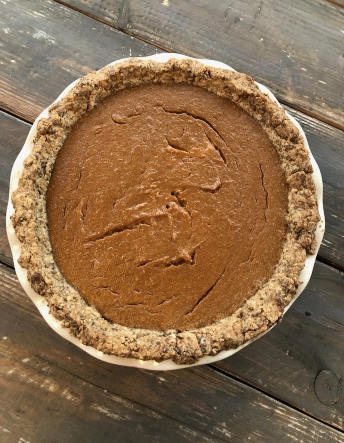 Pumpkin pie in a white dish with a crumbly crust, sitting on a wooden surface.