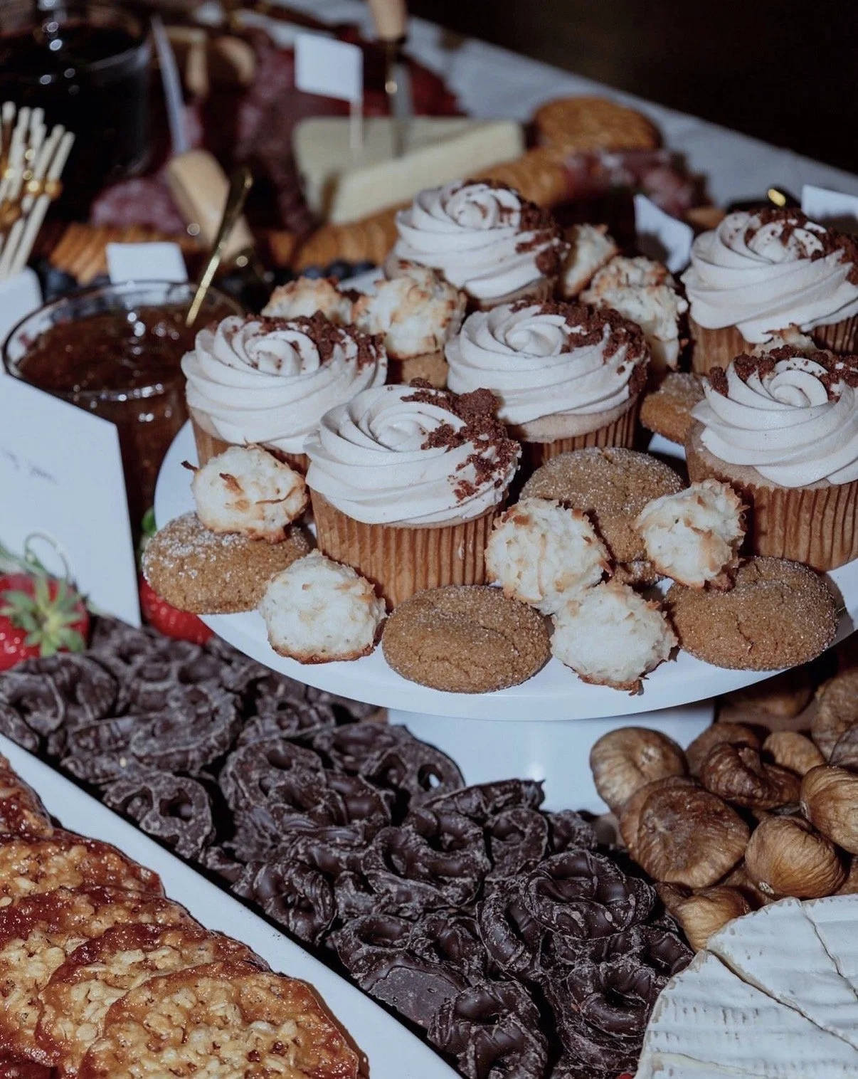 Assorted desserts including cupcakes with whipped frosting, cookies, chocolate-covered pretzels, and croissants on a dessert table.
