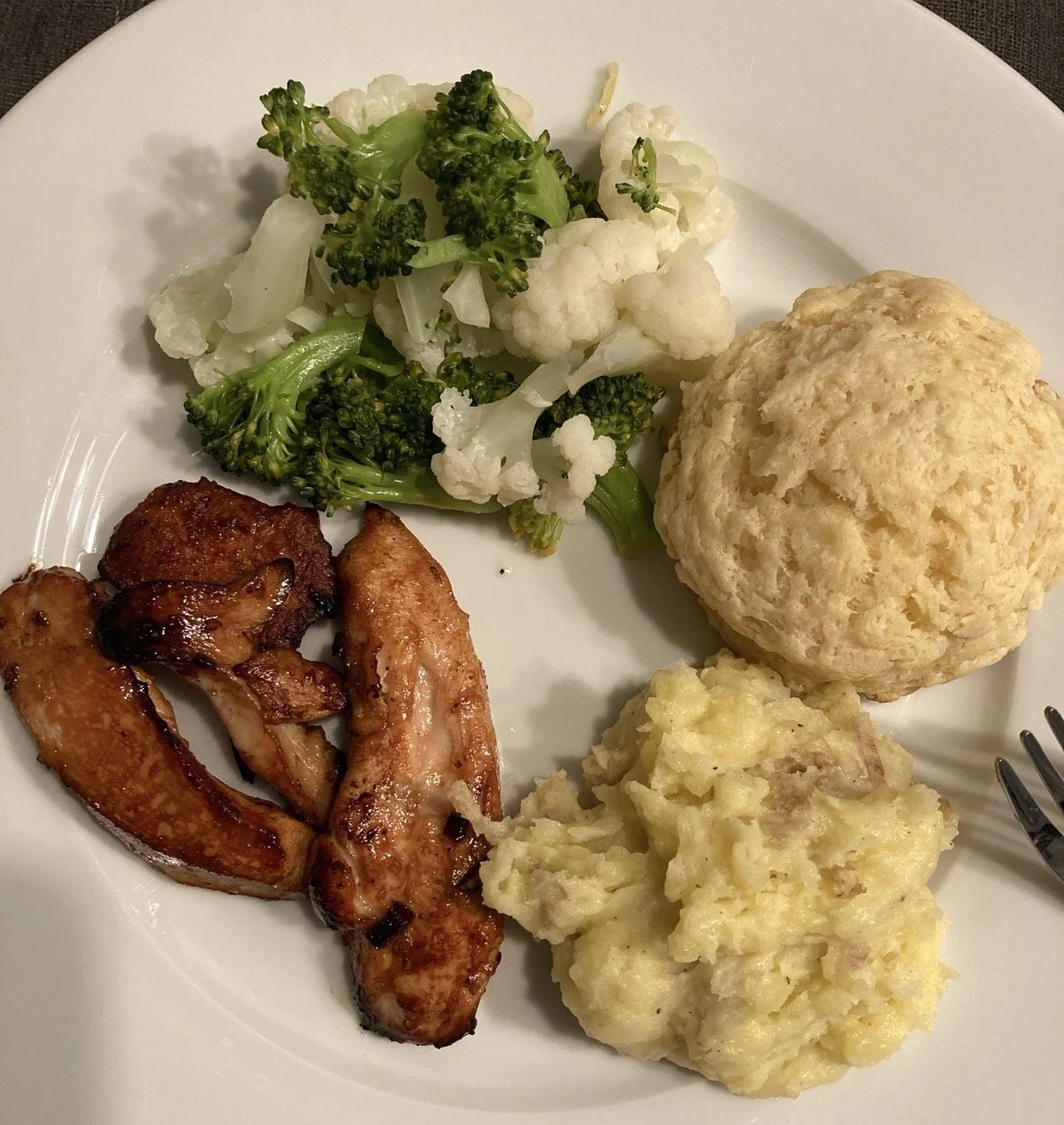 Plate of food with steamed broccoli and cauliflower, a baked biscuit, mashed potatoes, and chicken wings.