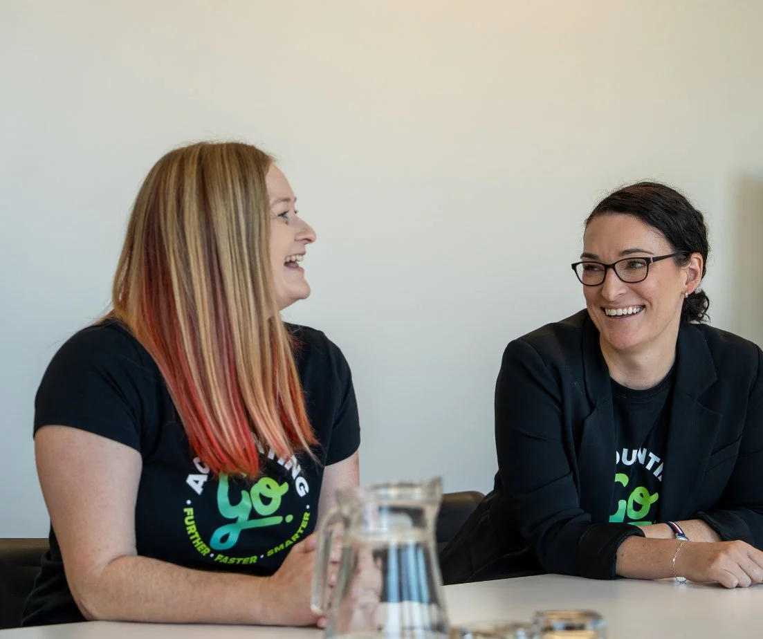 Two women from Go Accounting sitting at a table, smiling and laughing together during a conversation, with a pitcher of water in front of them.