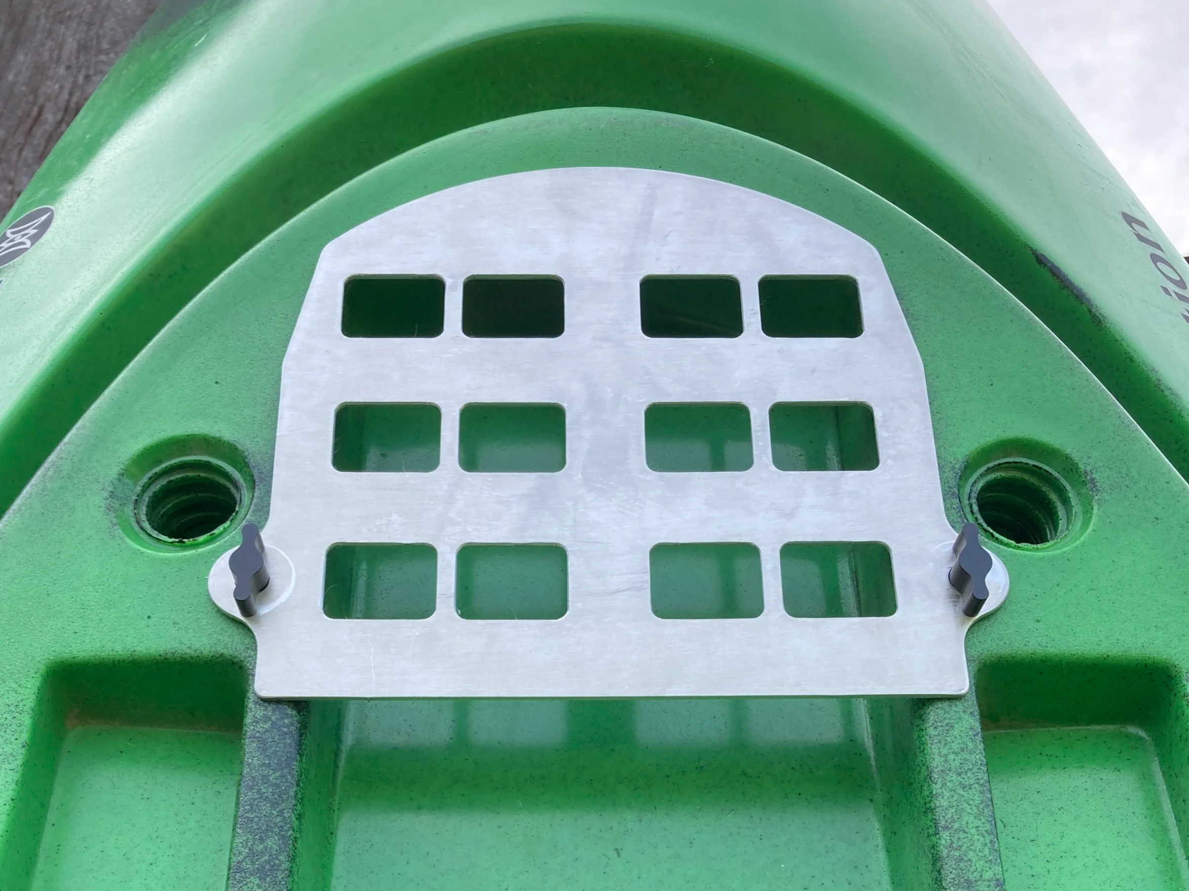 Close-up view of a green kayak with a silver metal plate featuring a grid pattern, attached to the kayak with small clips, with screw holes for mounting.