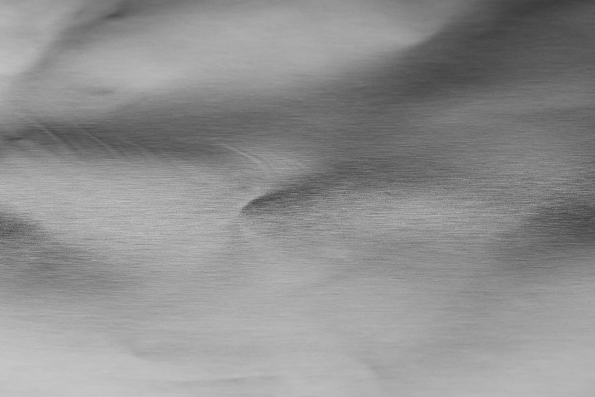 Abstract image showing a smooth, flowing pattern with shades of gray and subtle gradients, resembling a metallic or brushed surface.