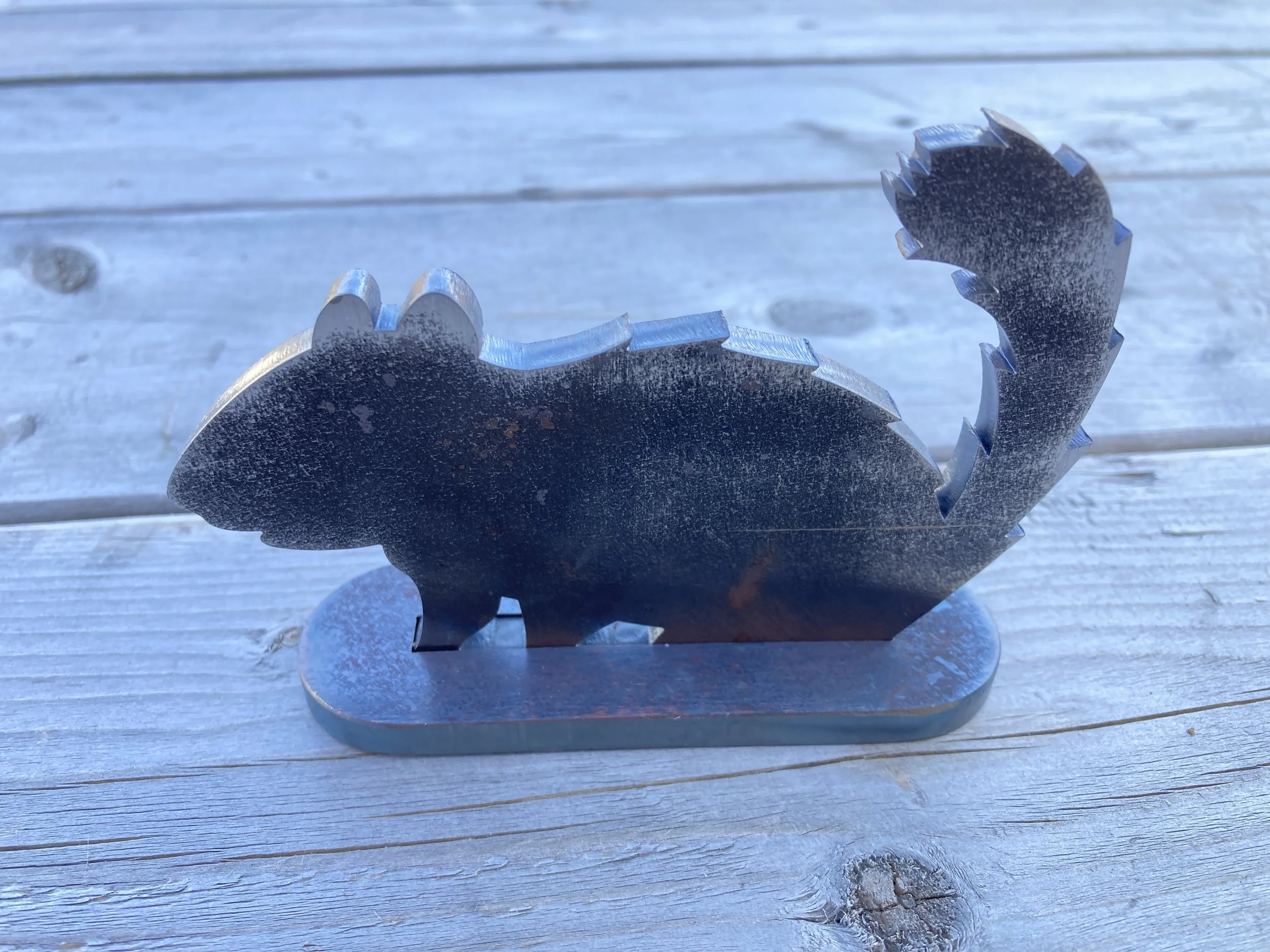 A metal sculpture of a squirrel on a wooden surface.