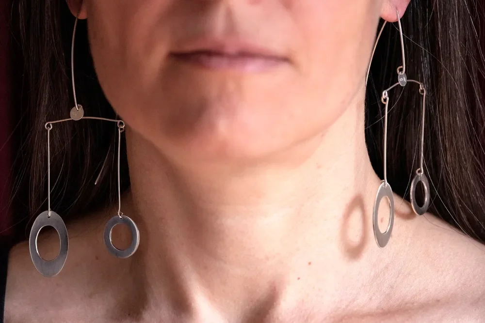 A woman wearing large, modern, silver geometric earrings with oval and circular shapes.
