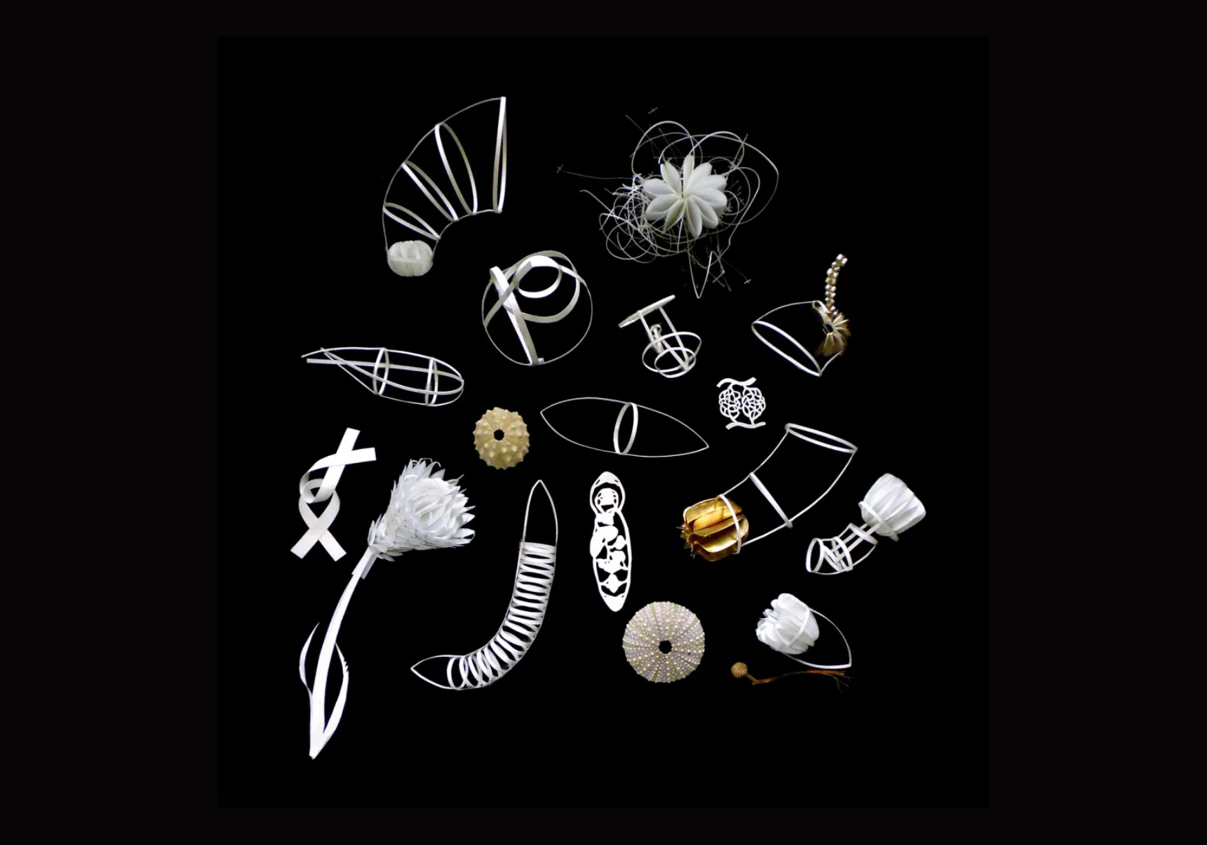 Collection of white decorative objects including paper flowers, wire sculptures, and intricate geometric designs on a black background.
