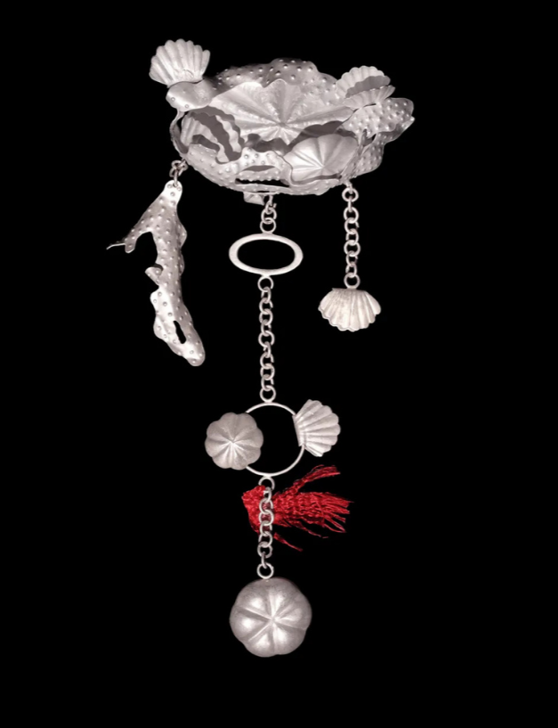 An artistic jewellery piece resembling a shell-shaped pendant with various decorative charms hanging from chains, set against a black background.