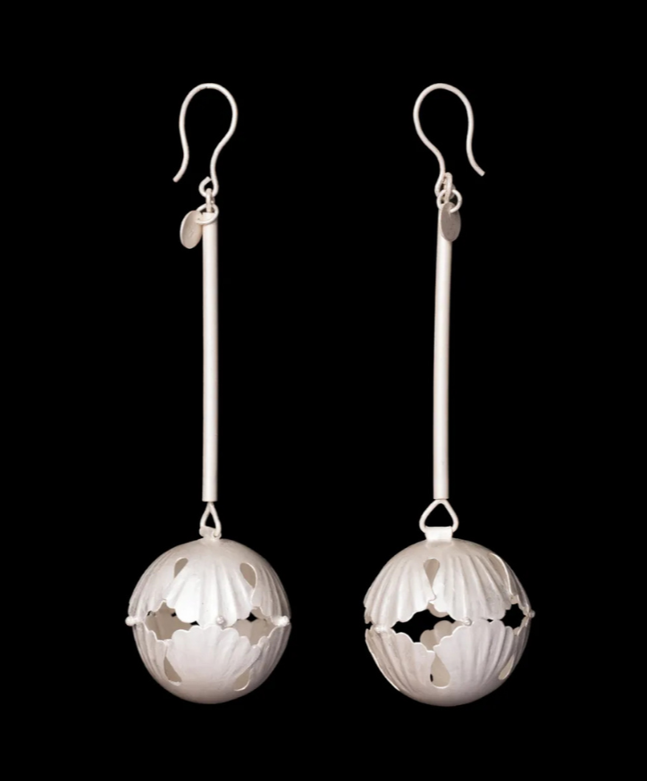 White spherical earrings with intricate cut-out patterns hanging from silver hooks against a black background.