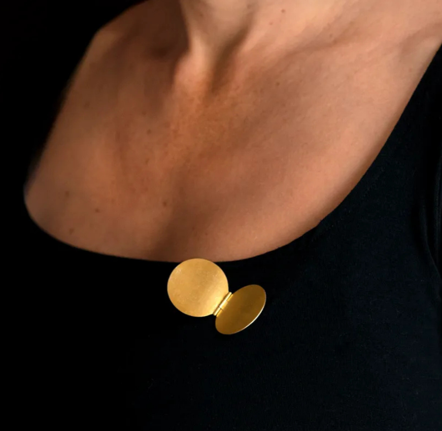 Close-up of a person’s neck and upper chest wearing a black top, with a gold brooch attached near the collar.